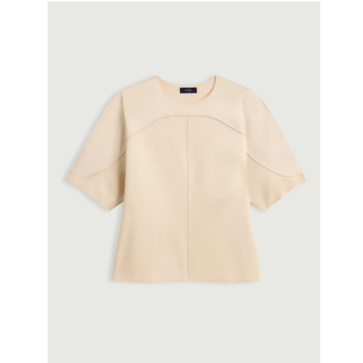 A light beige short-sleeve knit top with structured shoulder panels and a central seam, displayed flat against a light gray background.