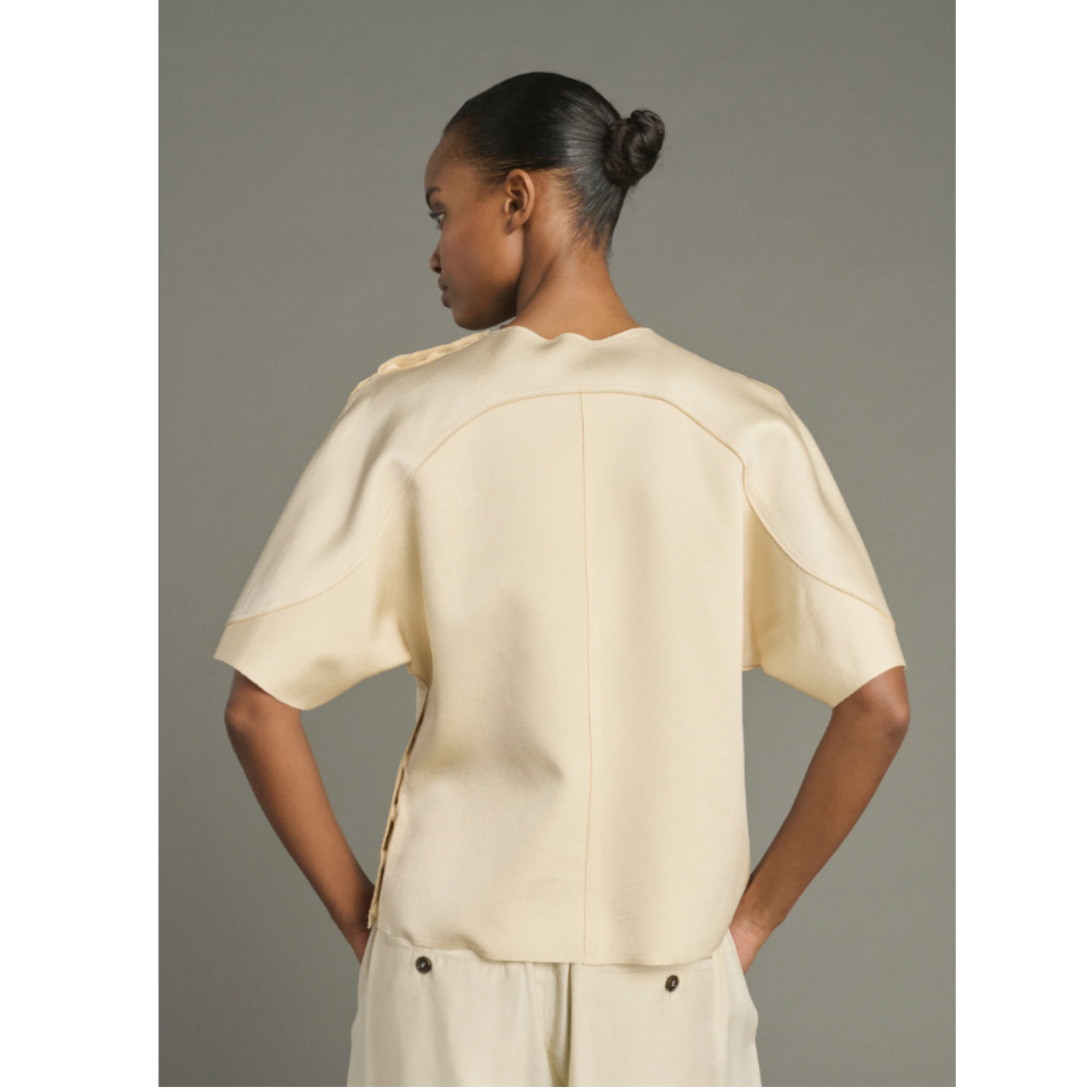 A model wearing a cream-colored short-sleeve top and matching wide-leg trousers against a solid gray studio background.