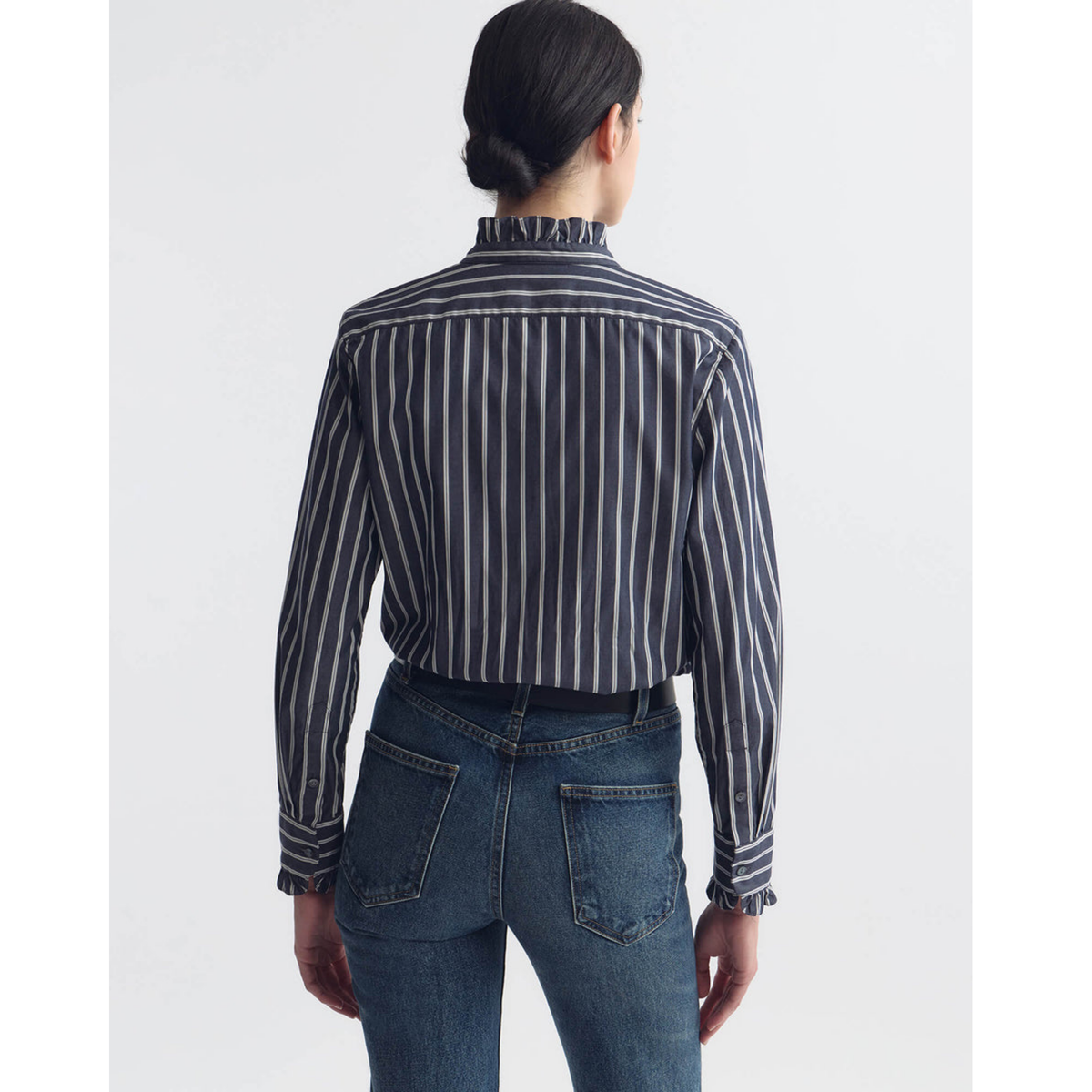Person wearing a black and white striped shirt and blue jeans on a light gray background