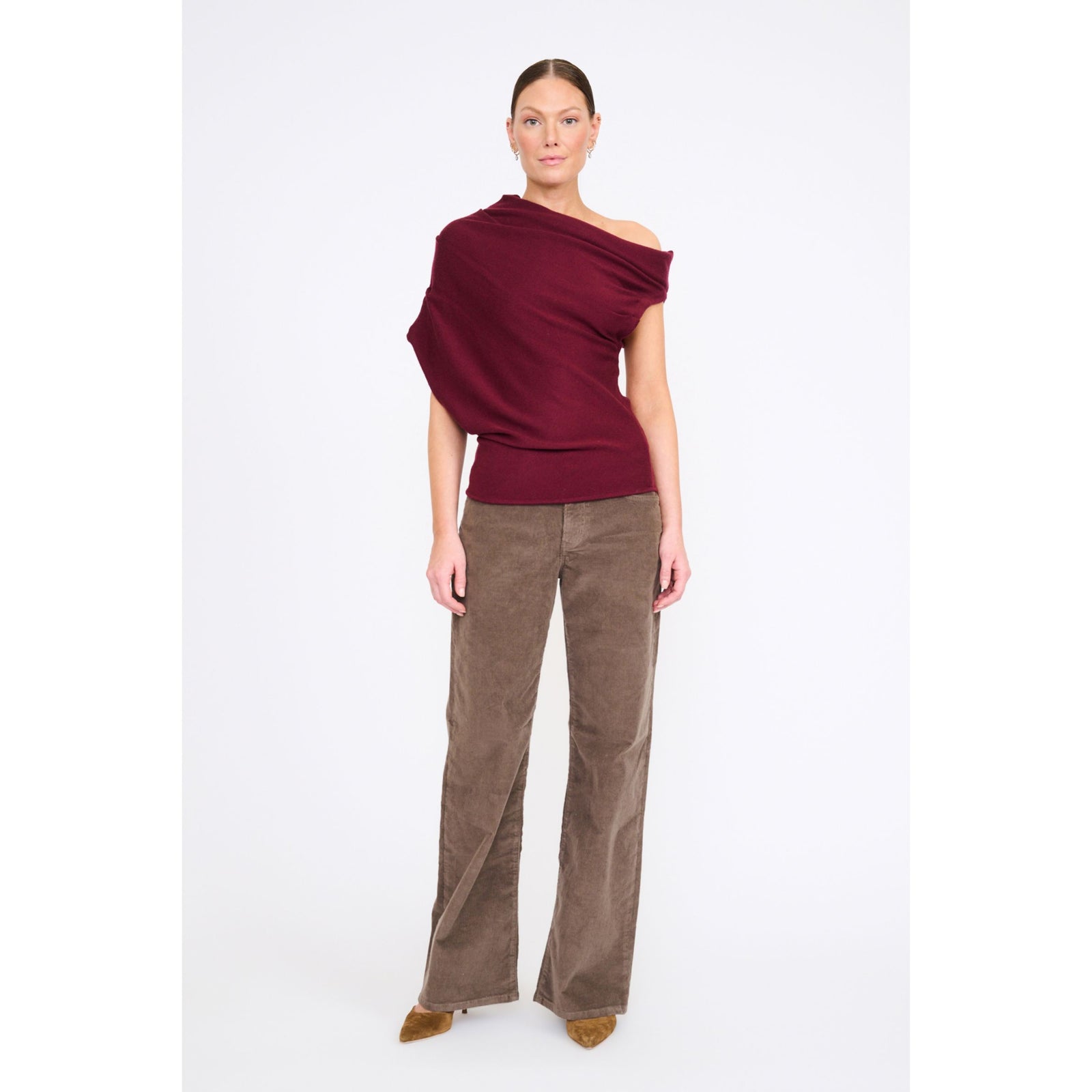 Woman in a red off the shoulder knit top with brown pants in front of a gray background