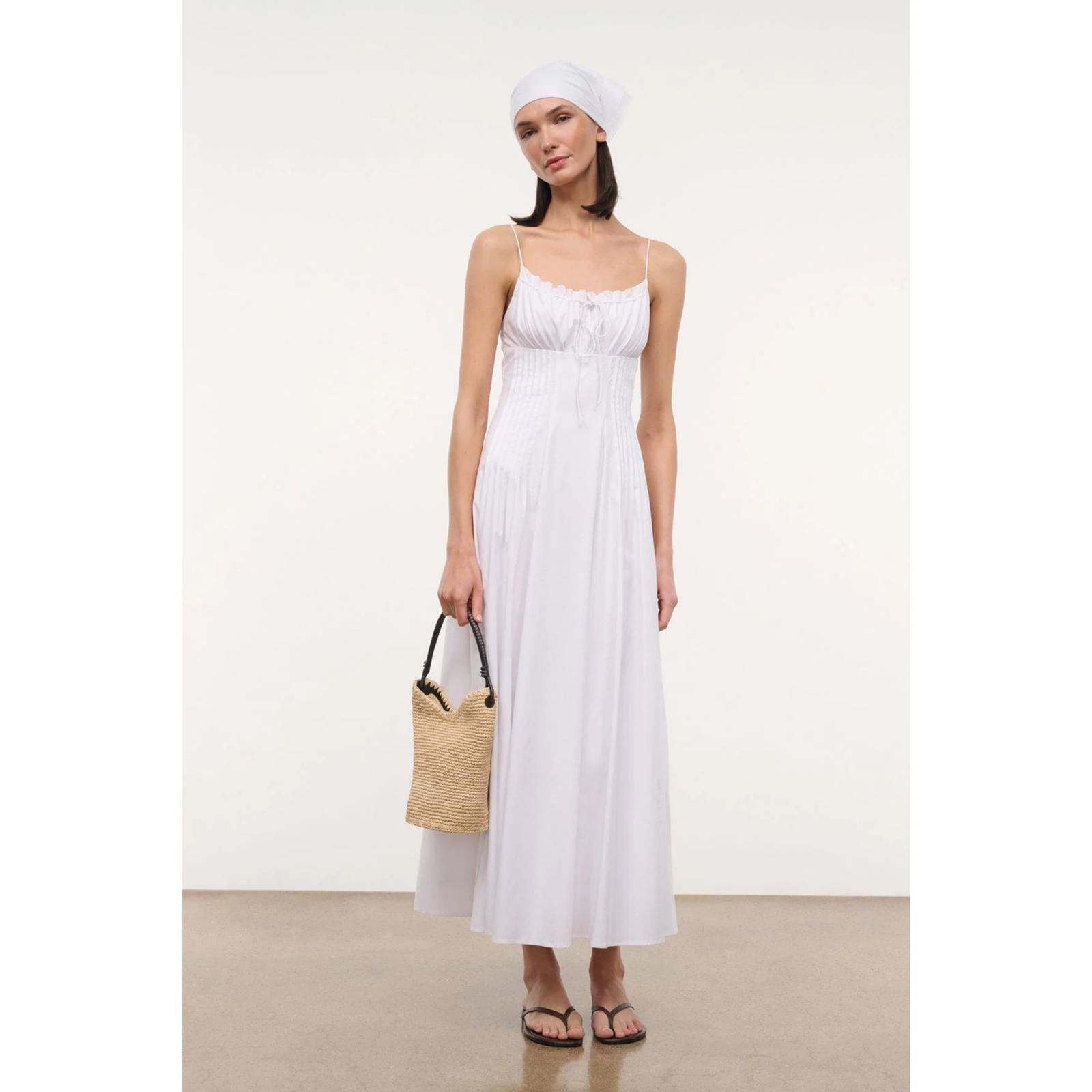 Woman wearing a white dress holding a straw bag on a plain background