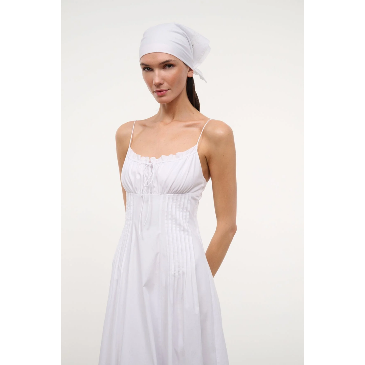 Woman wearing a white dress and headscarf on a plain background