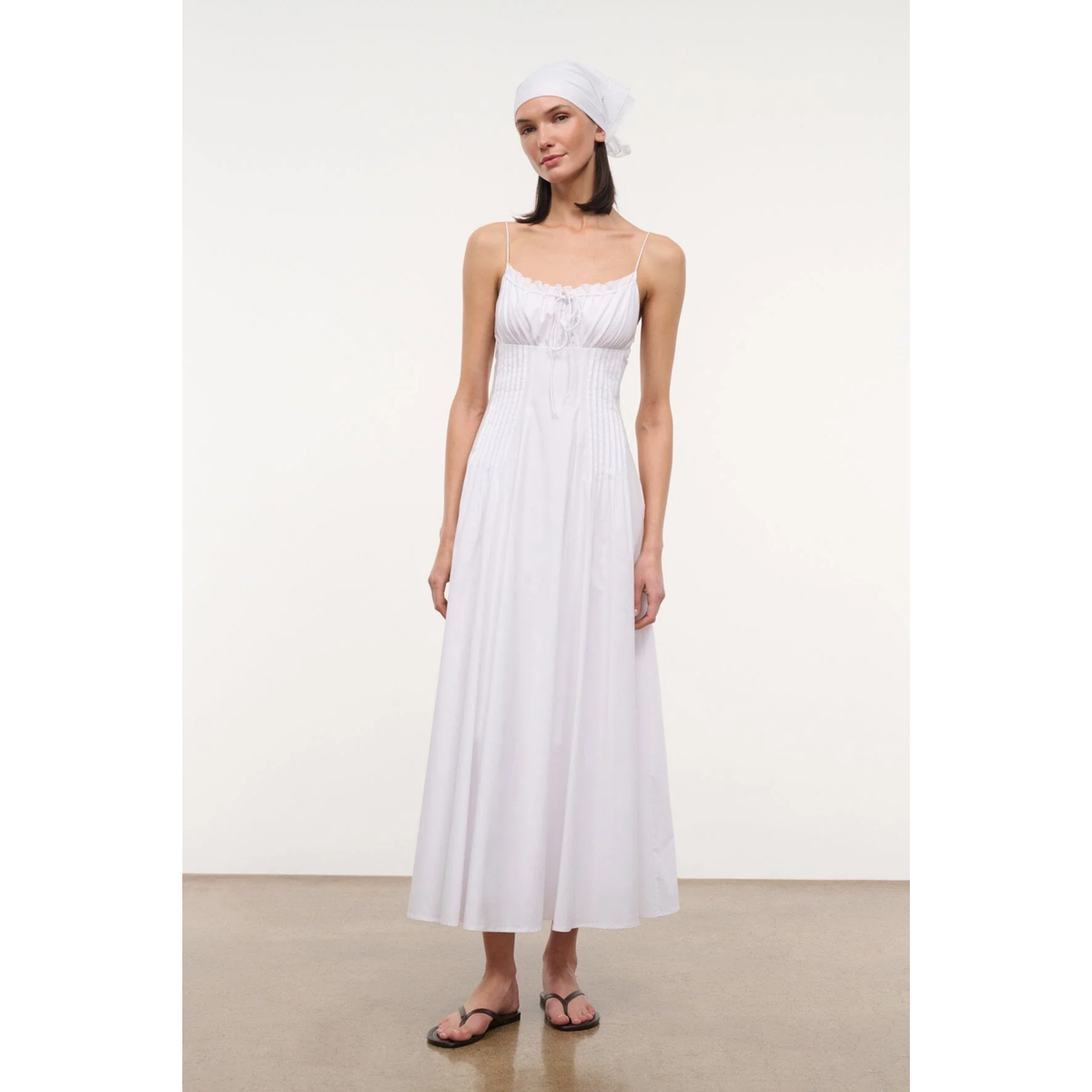 Woman wearing a white dress and headscarf on a plain background