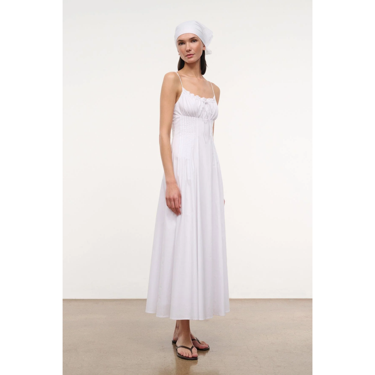 Woman wearing a white dress and headscarf on a plain background