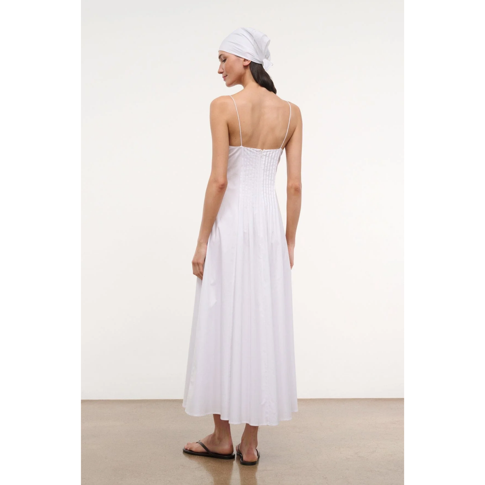 Woman wearing a white dress holding a straw bag on a plain background