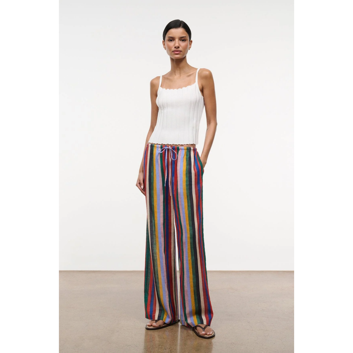 Woman wearing a white top and colorful striped pants on a plain background