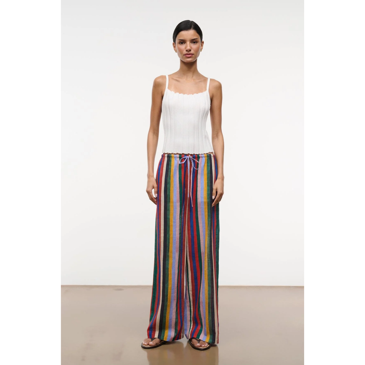 Woman wearing a white top and colorful striped pants on a plain background