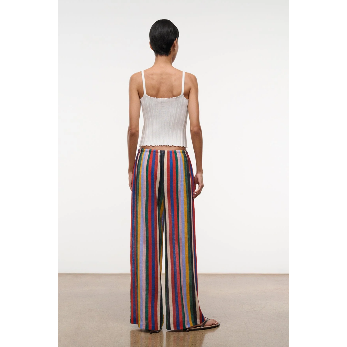 Woman wearing a white top and colorful striped pants on a plain background