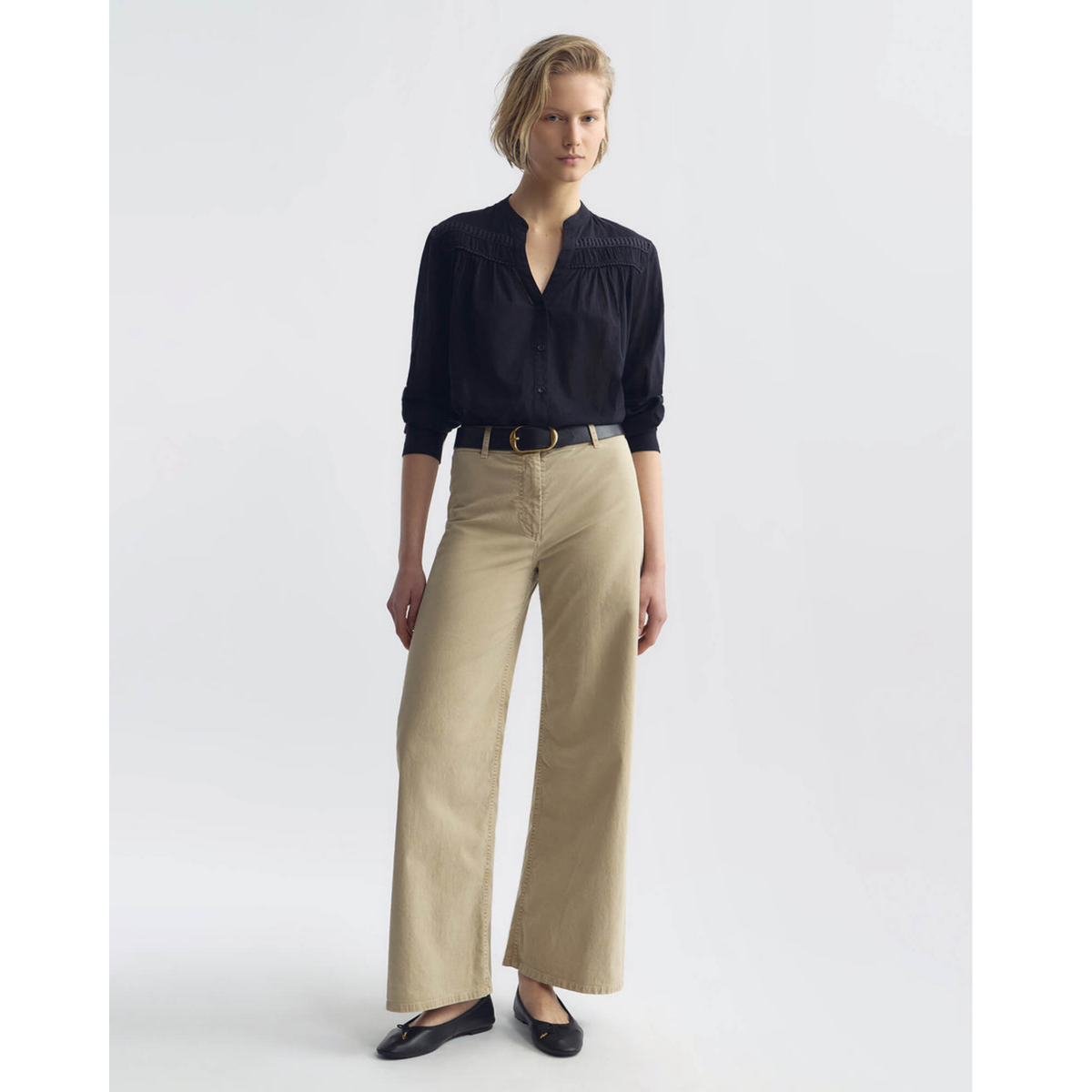 Woman wearing a black blouse and beige pants on a white background