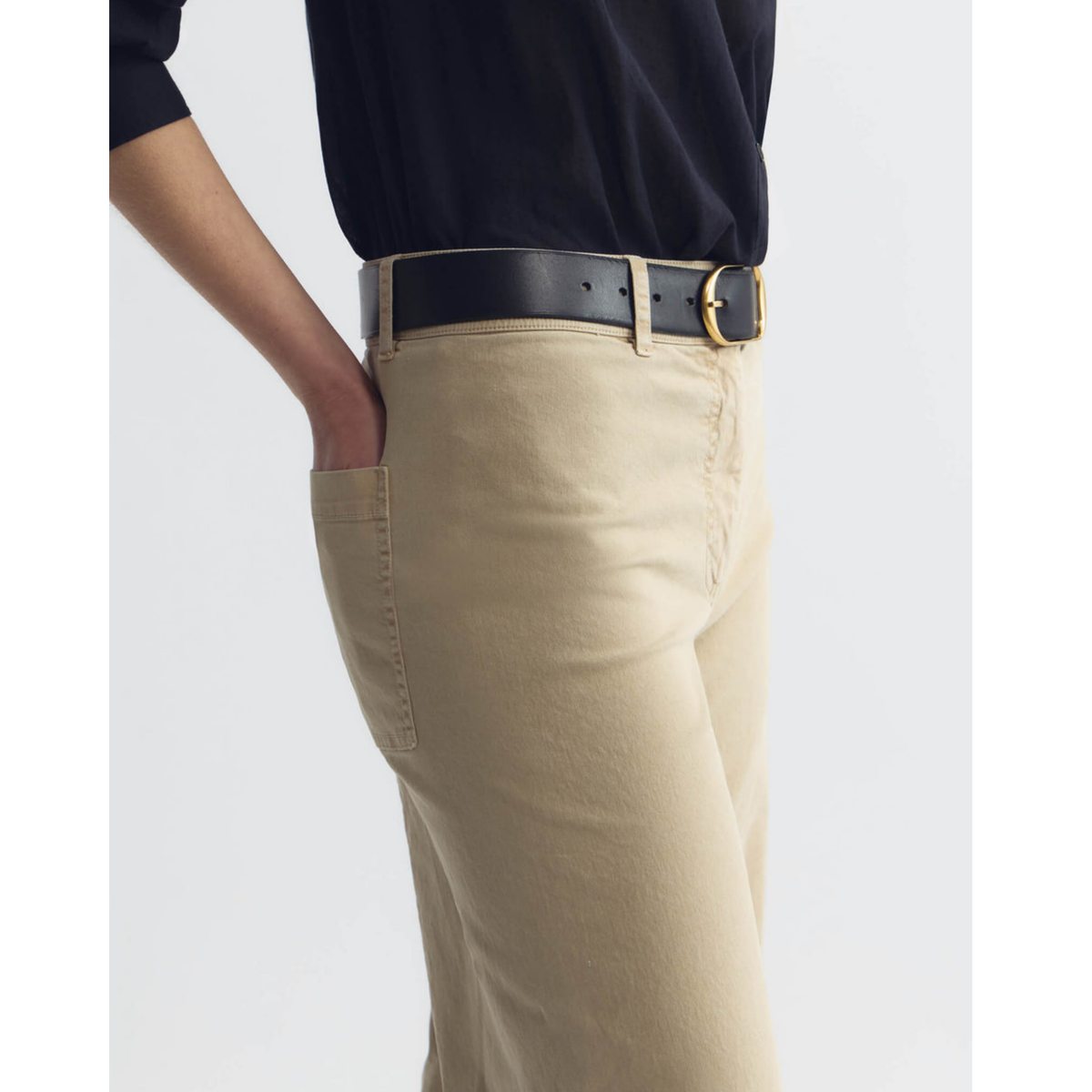 Person wearing beige pants with a black belt on a white background