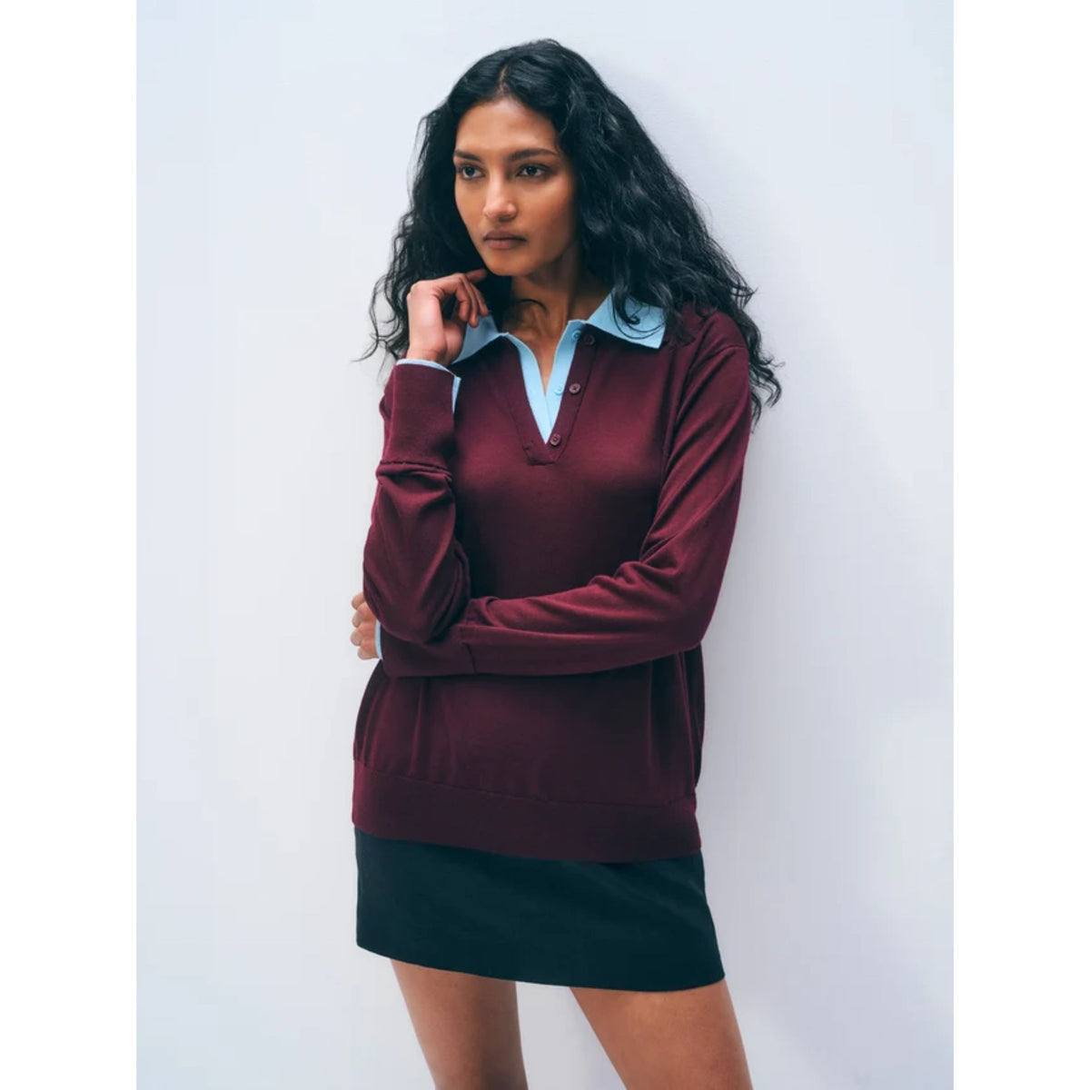 Front waist-up view of a model wearing the burgundy knit polo sweater with a light blue contrast collar and dark bottom.