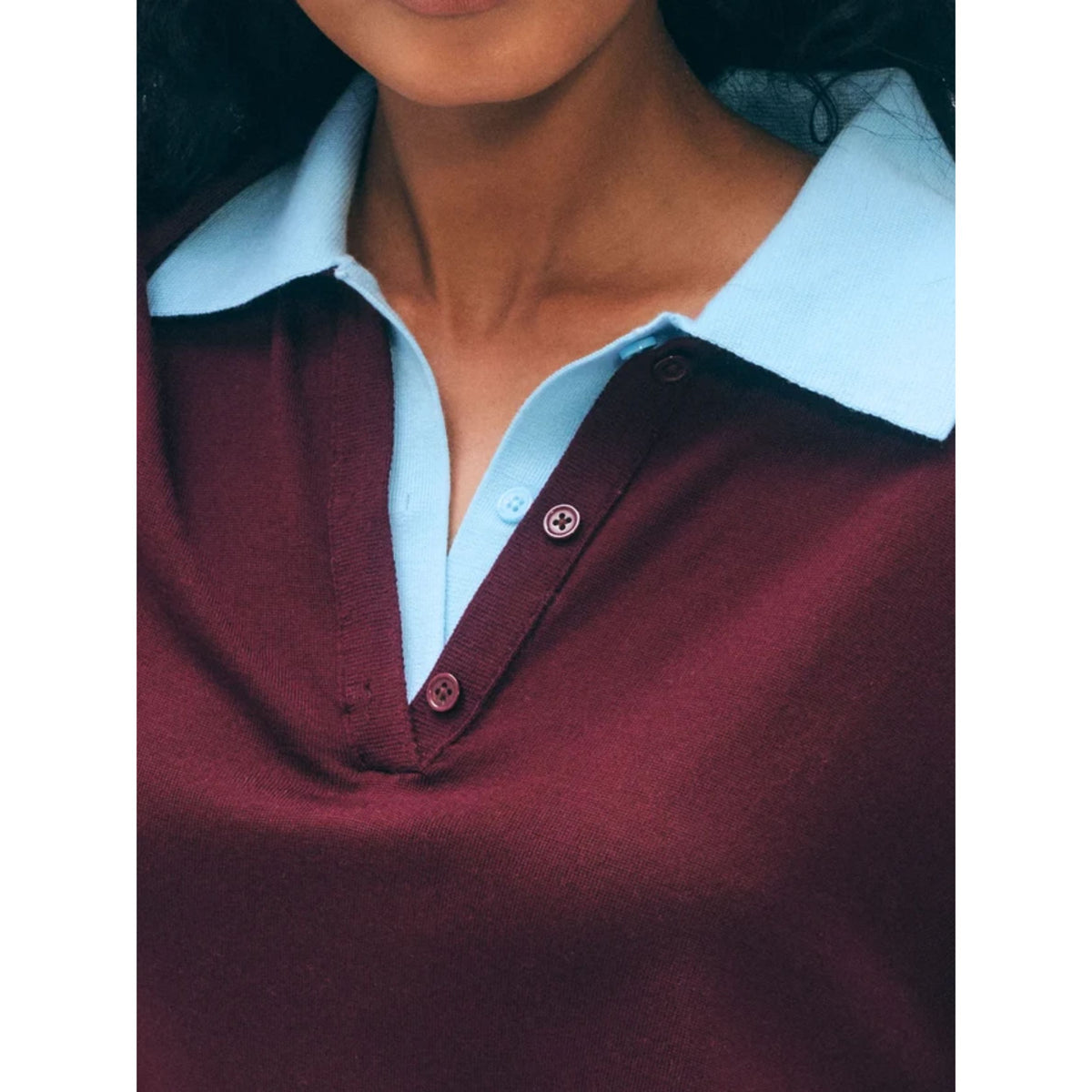 Close-up shot of the open v-neckline, button placket, and light blue contrast collar on the burgundy knit merino polo sweater.