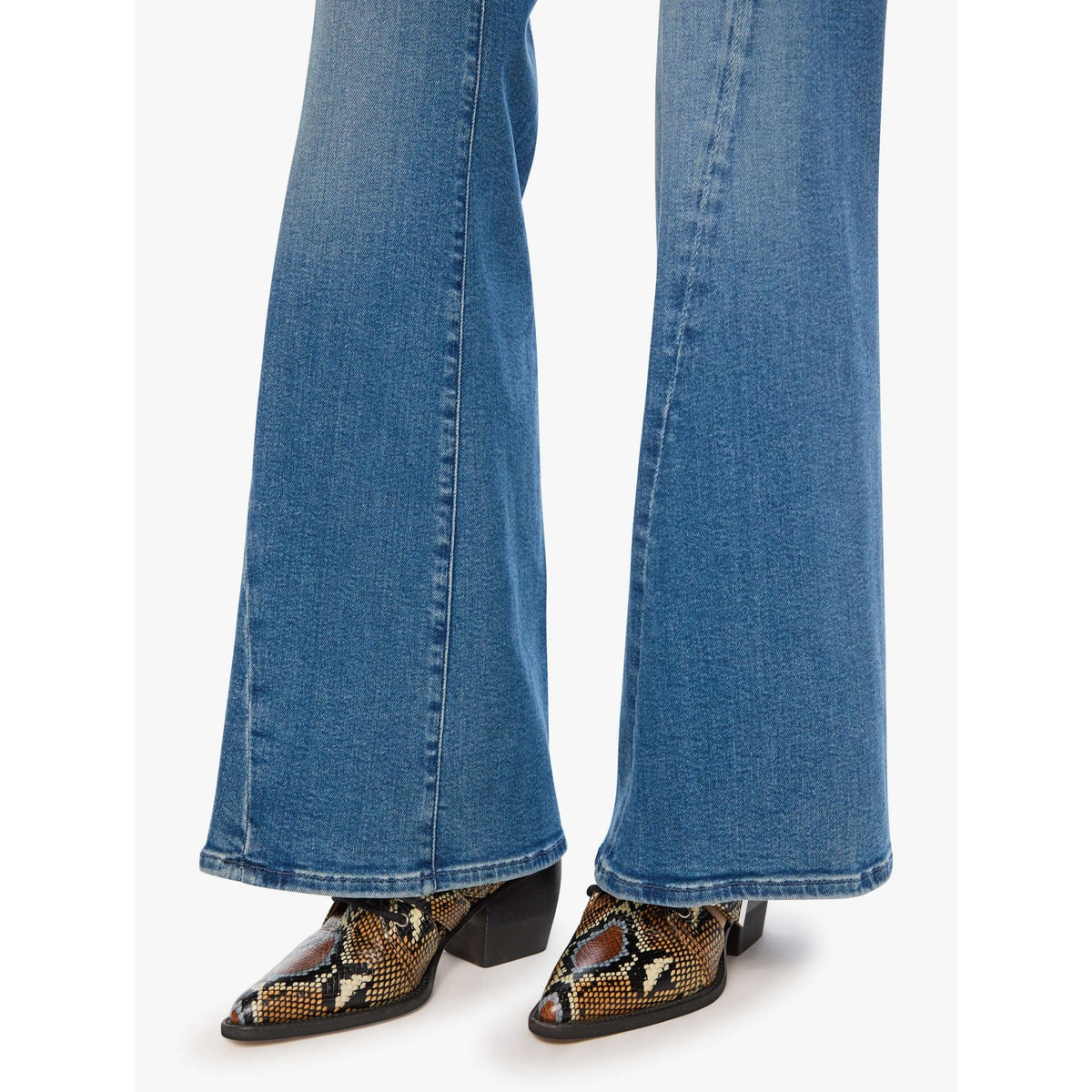Close-up of a person's legs wearing medium-wash blue flared jeans and pointed-toe snakeskin boots with black heels, shown against a plain light background.