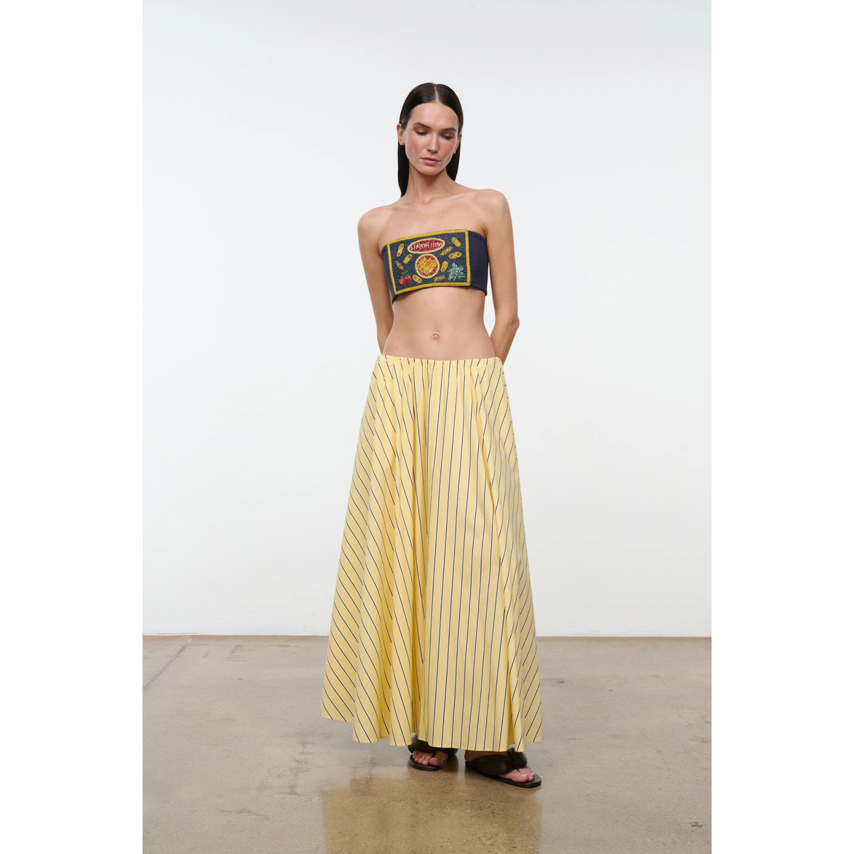 Woman wearing a strapless top with a graphic design and a long yellow striped skirt on a white background