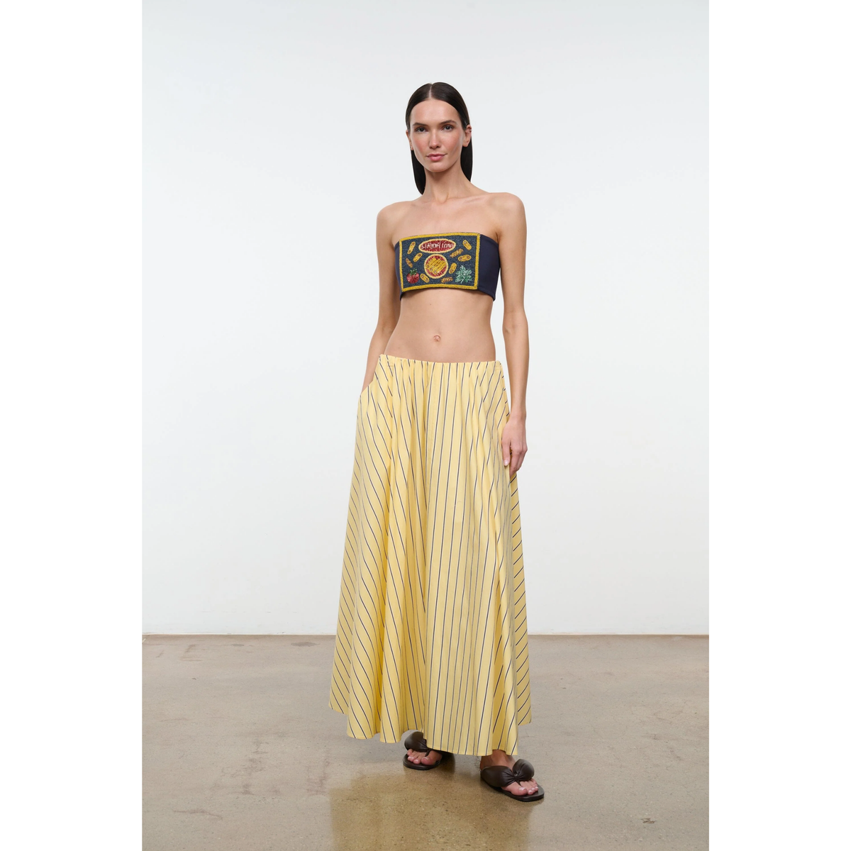 Woman wearing a strapless top with a colorful design and a long yellow skirt on a white background
