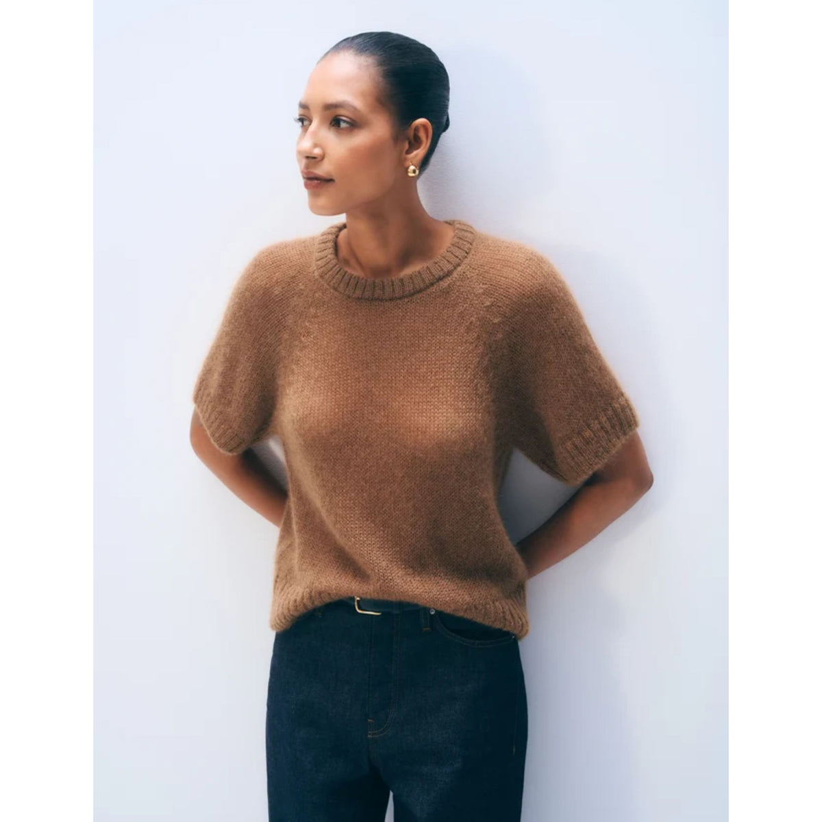 Waist-up shot of a model wearing the short-sleeve Camel brown mohair blend knit tee with hands on hips, styled with dark pants.