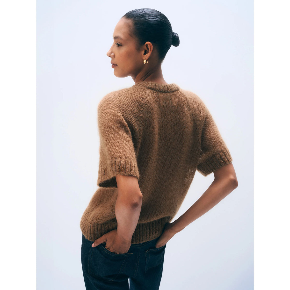 Back view of a model wearing the short-sleeve Camel brown mohair-blend knit tee paired with dark trousers.
