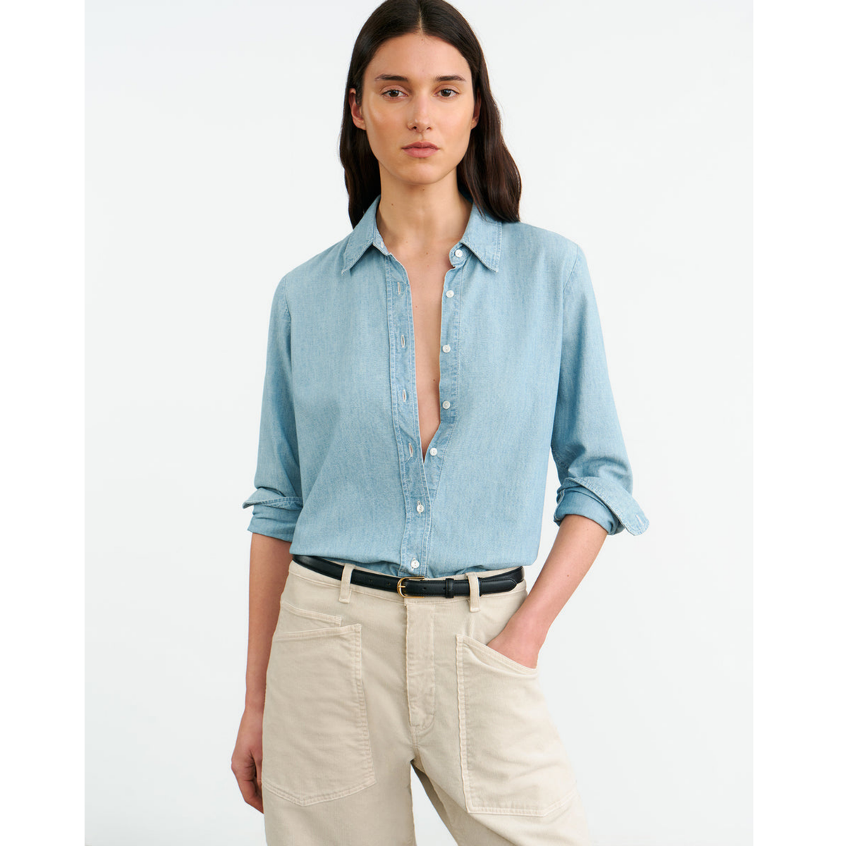 Woman wearing a light blue denim shirt and beige pants on a white background