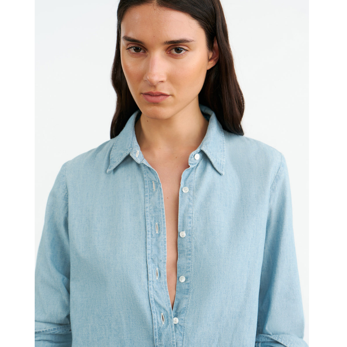 Woman wearing a light blue denim shirt on a white background