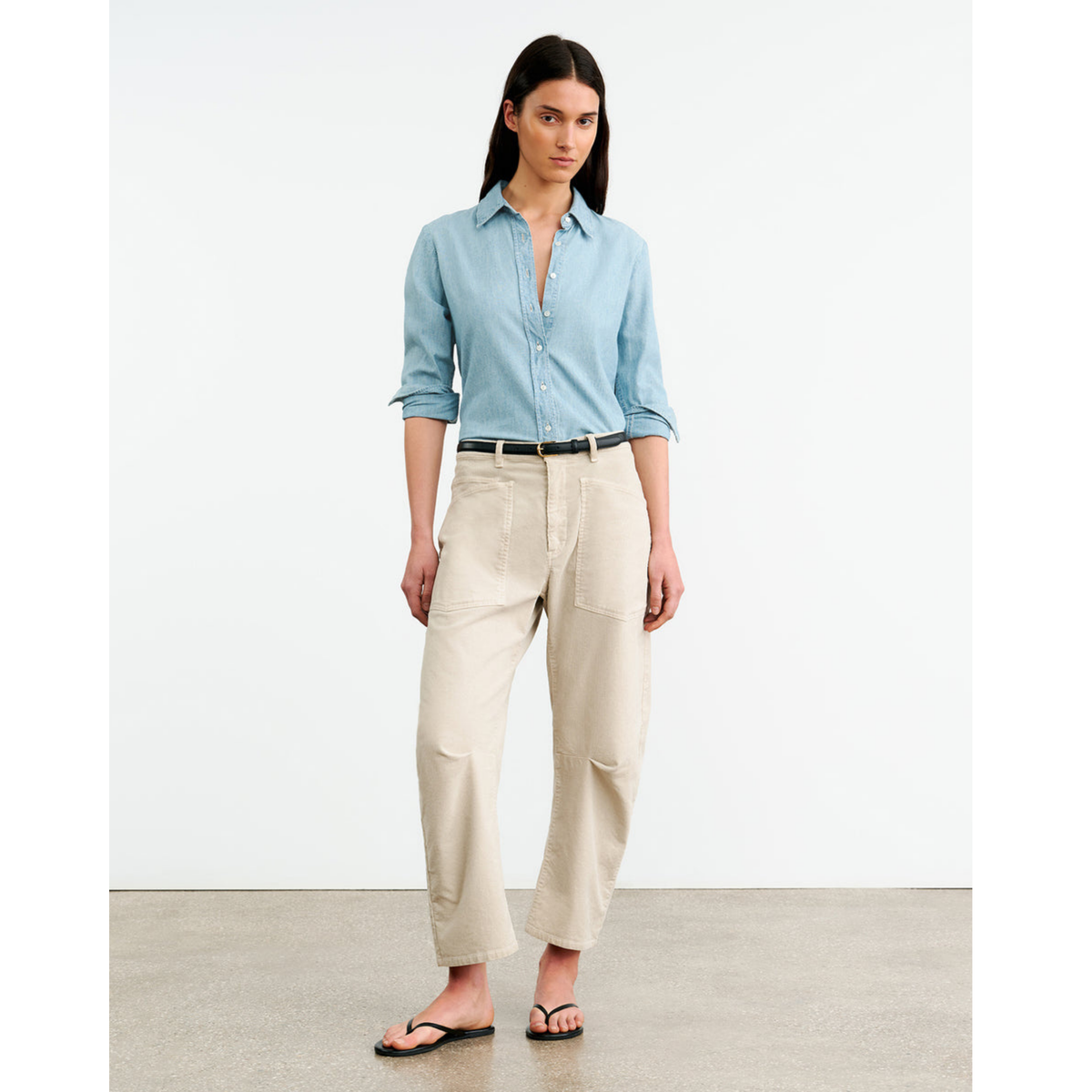 Woman wearing a light blue shirt and beige pants on a plain background