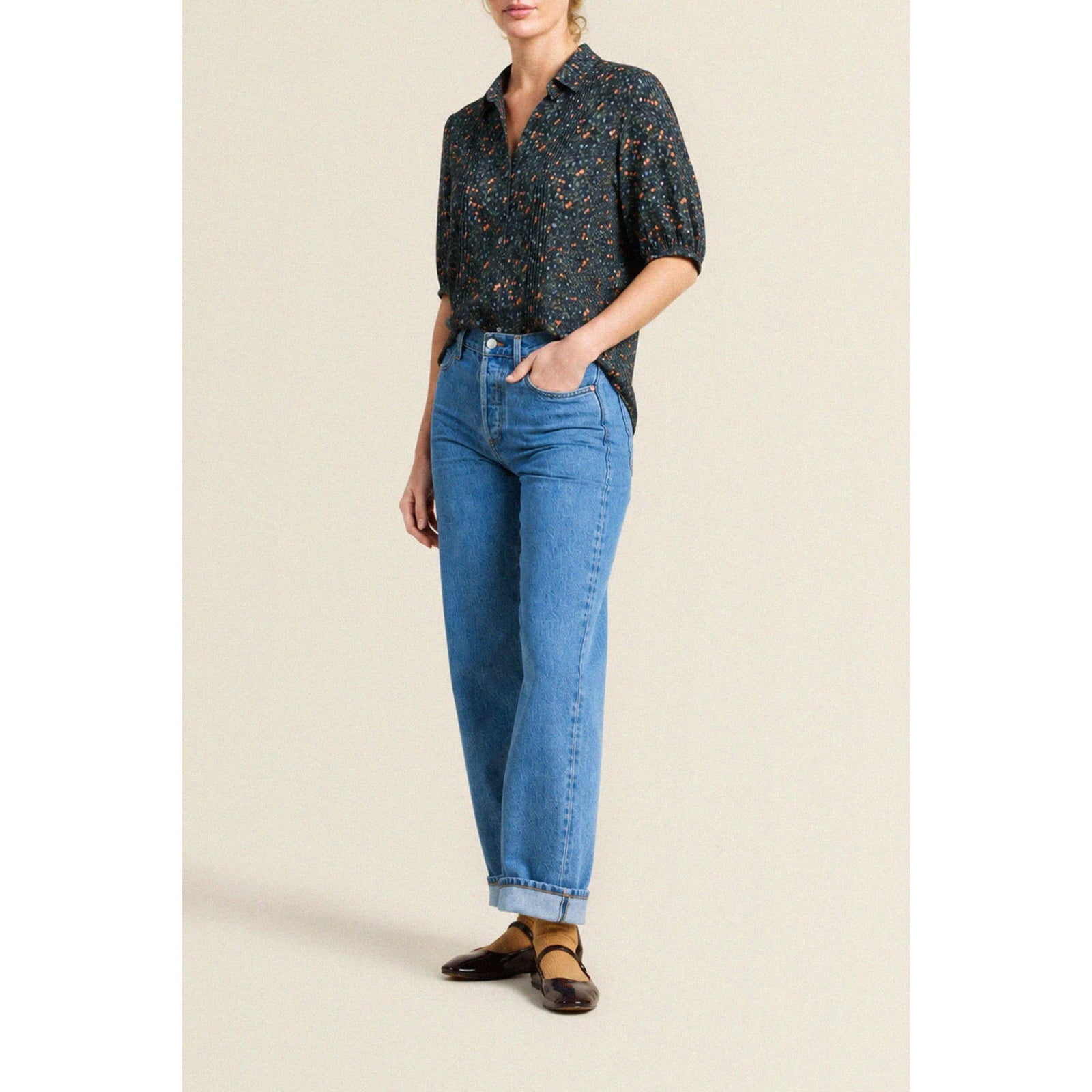 A short-sleeve blouse with a dark navy blue base and a dense orange and yellow floral print, featuring puff sleeves and a small bow at the collar, displayed flat against a light beige background.