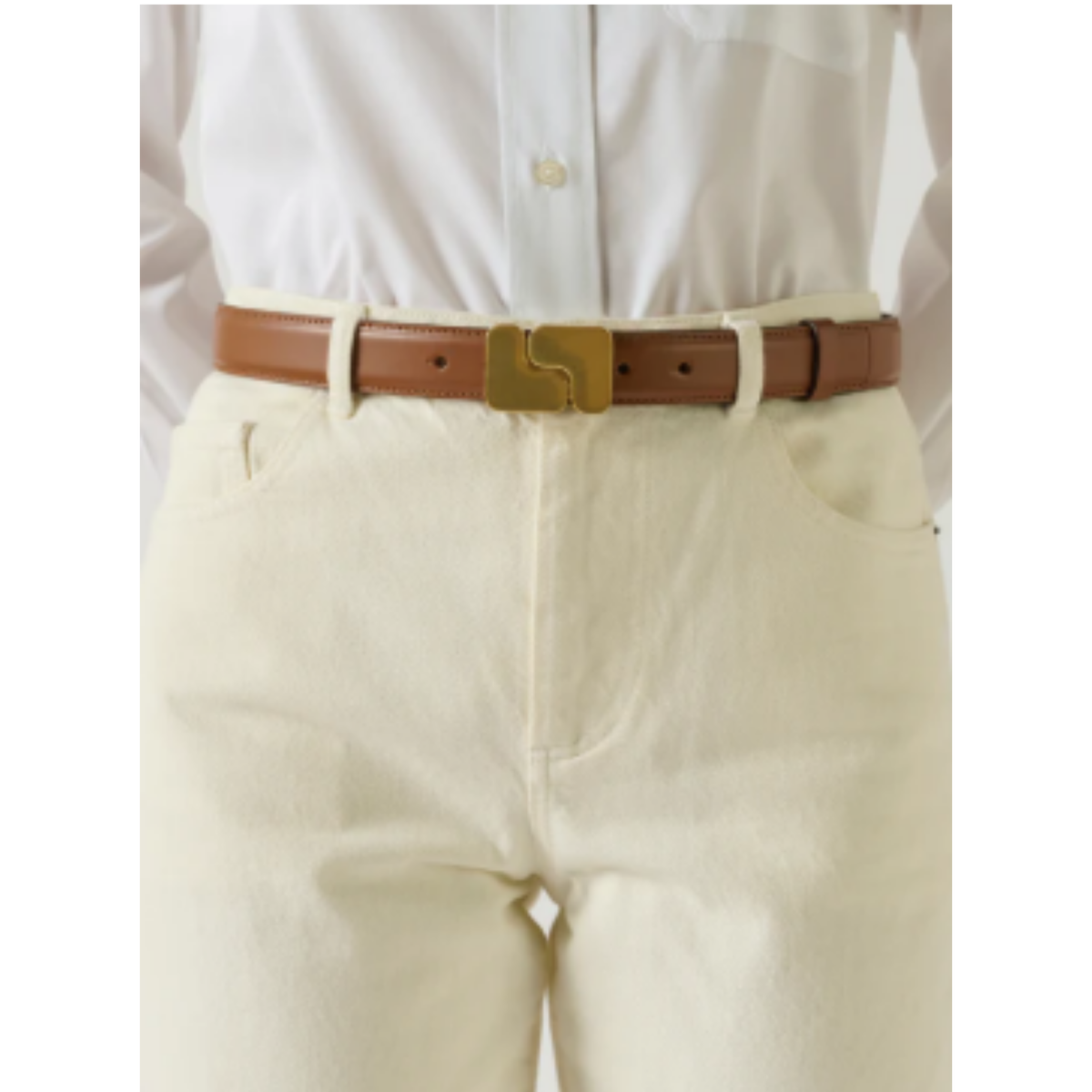 A close-up of a person wearing a brown leather belt with a gold-tone buckle, paired with off-white trousers and a white button-up shirt.