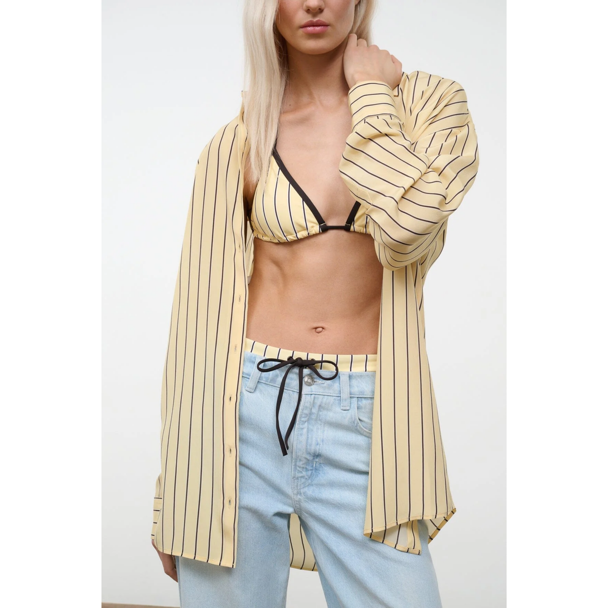 Person wearing a striped shirt over a bikini top and light blue pants on a white background