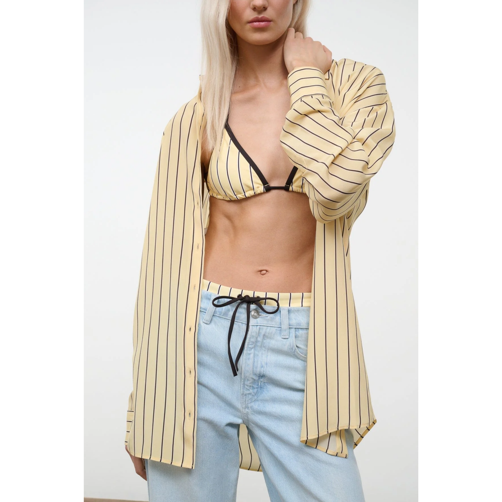 Woman wearing a yellow striped shirt, black bikini top, and light blue jeans with a white background