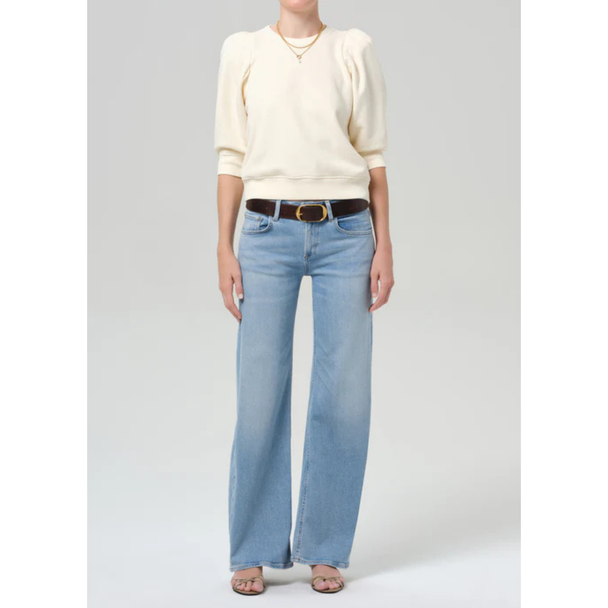Person wearing a cream sweater and light blue jeans on a gray background