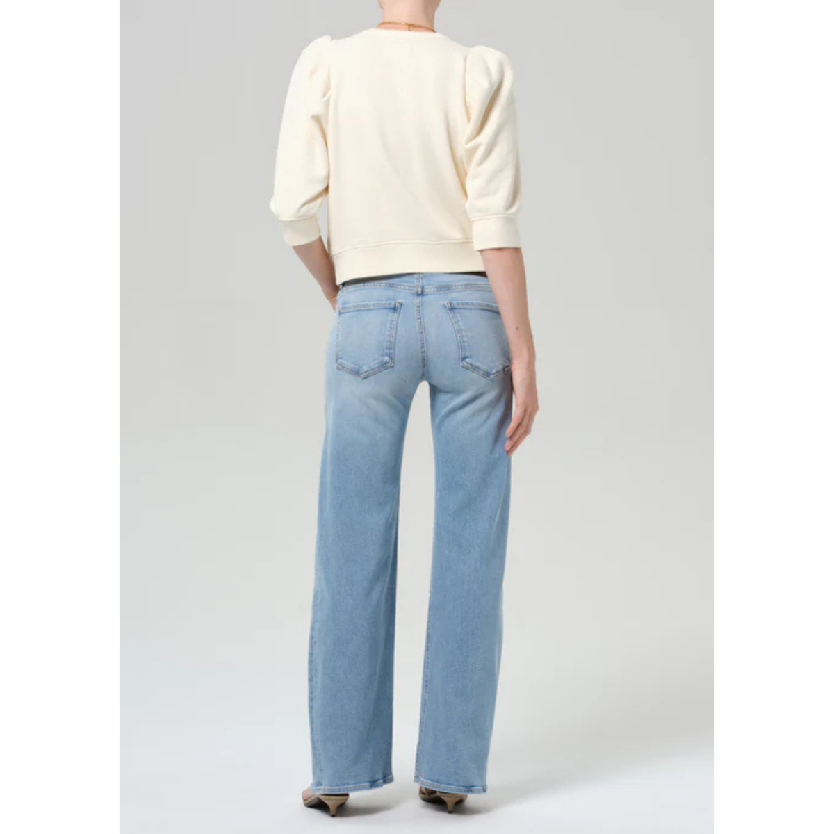 Person wearing light blue jeans and a cream sweater on a gray background