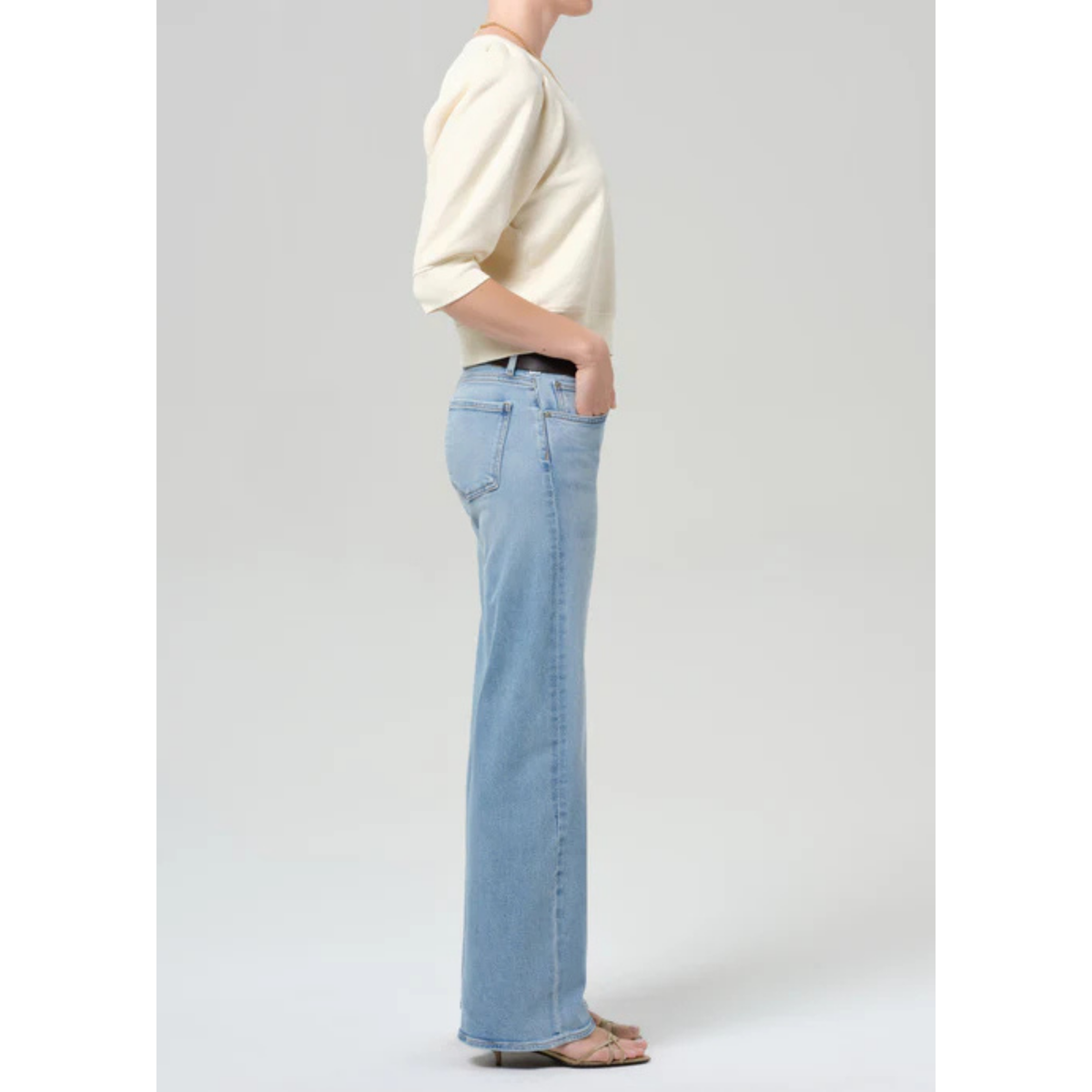 Person wearing light blue jeans and a cream sweater on a plain background