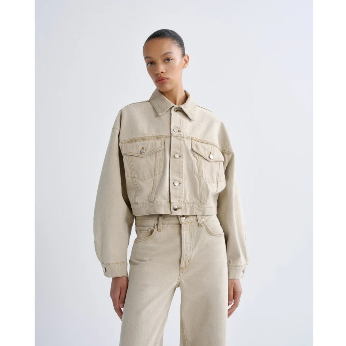 Front three-quarters view of a model wearing the cropped AGOLDE Palmer Jacket in Arena with long balloon sleeves, paired with matching sandy khaki jeans against a light gray background.