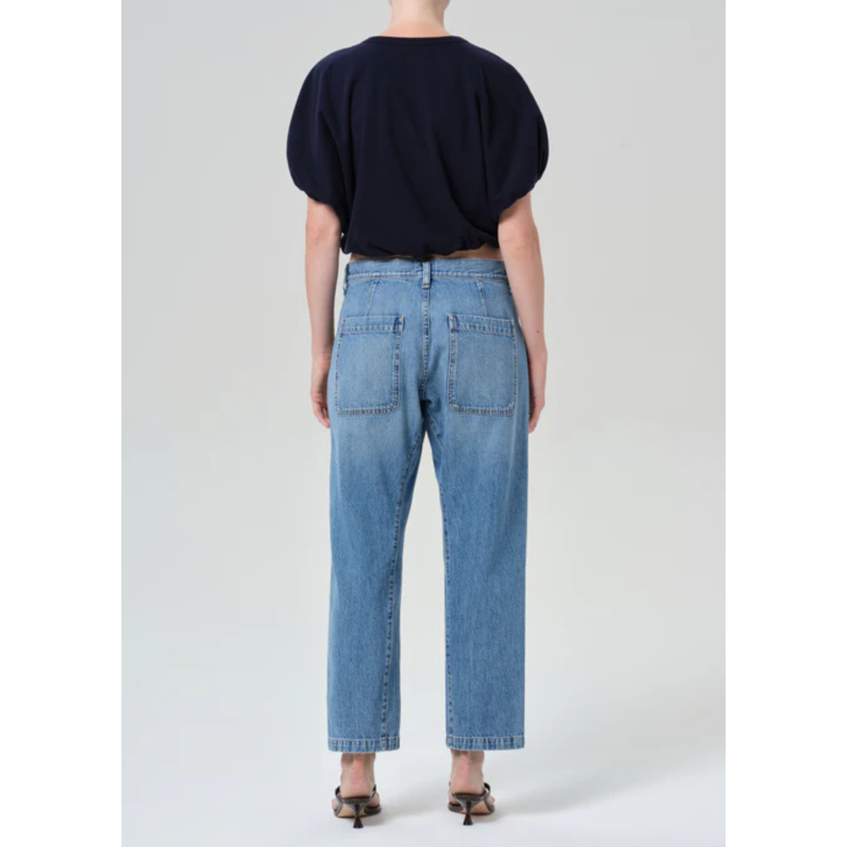 Person wearing blue jeans and a black top on a white background