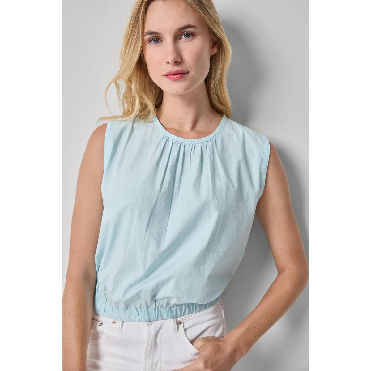 Woman wearing a light blue sleeveless top against a plain background