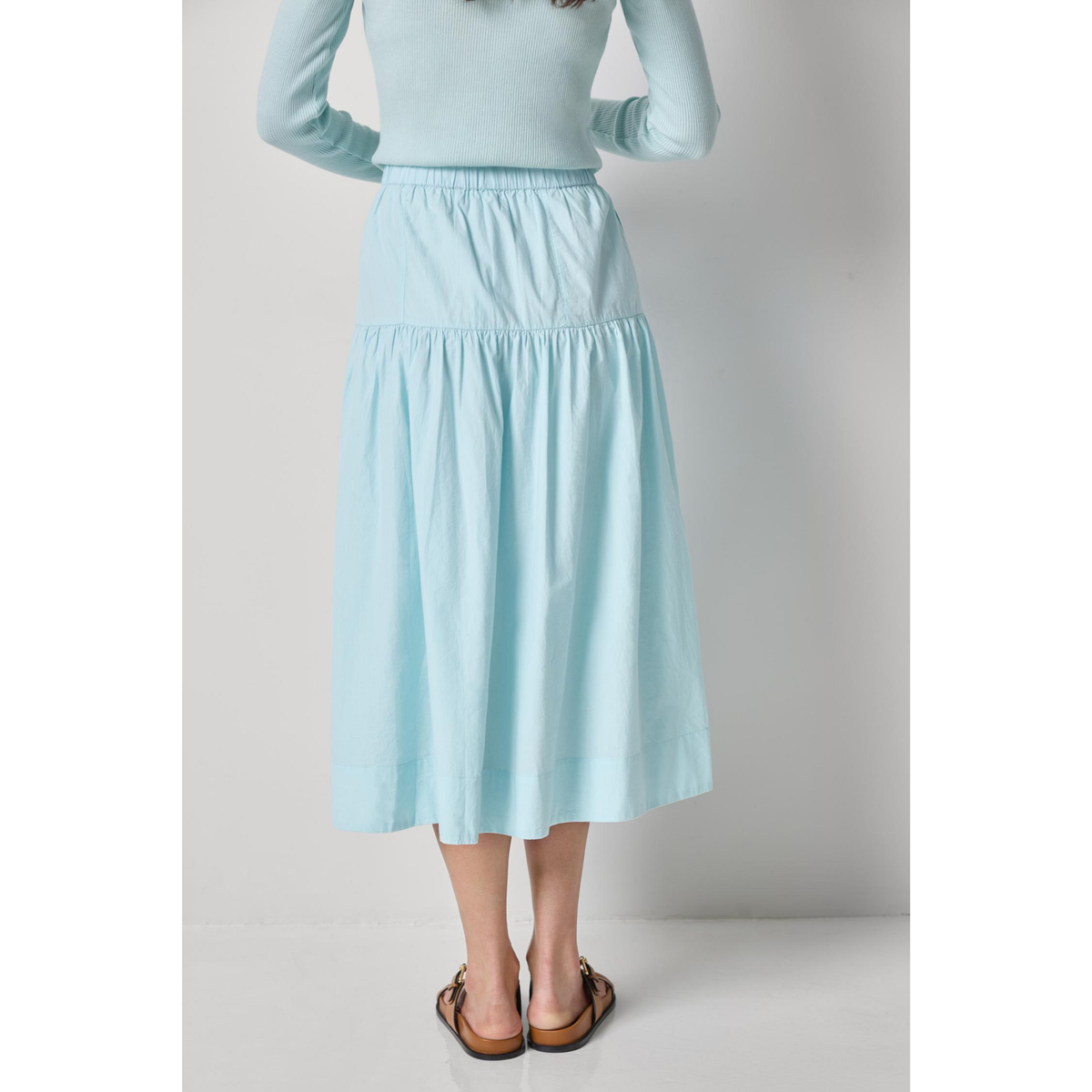 Person wearing a light blue skirt with a plain background