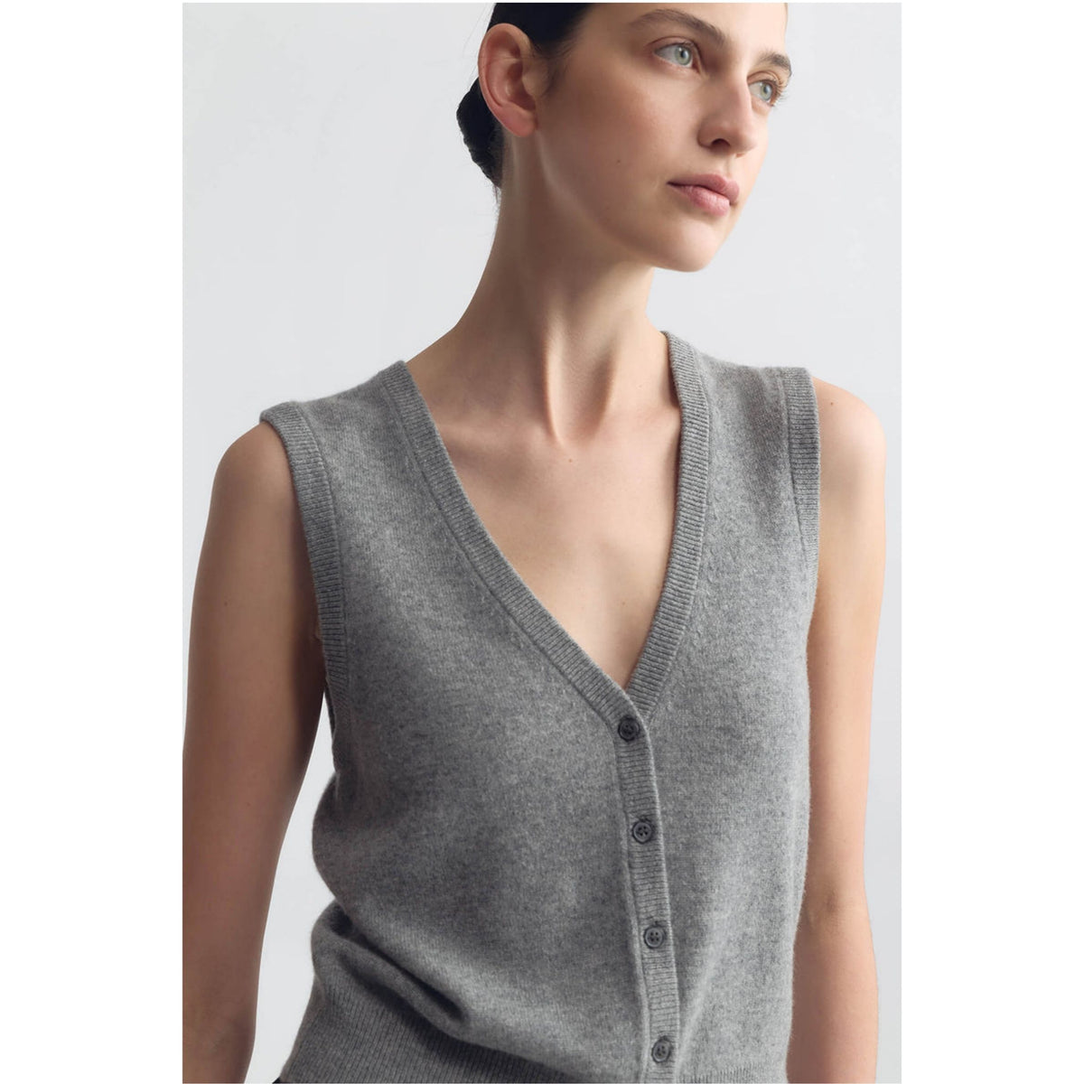 A woman wearing a sleeveless gray knit cardigan vest with a V-neck and dark buttons, shown against a plain light gray studio background.