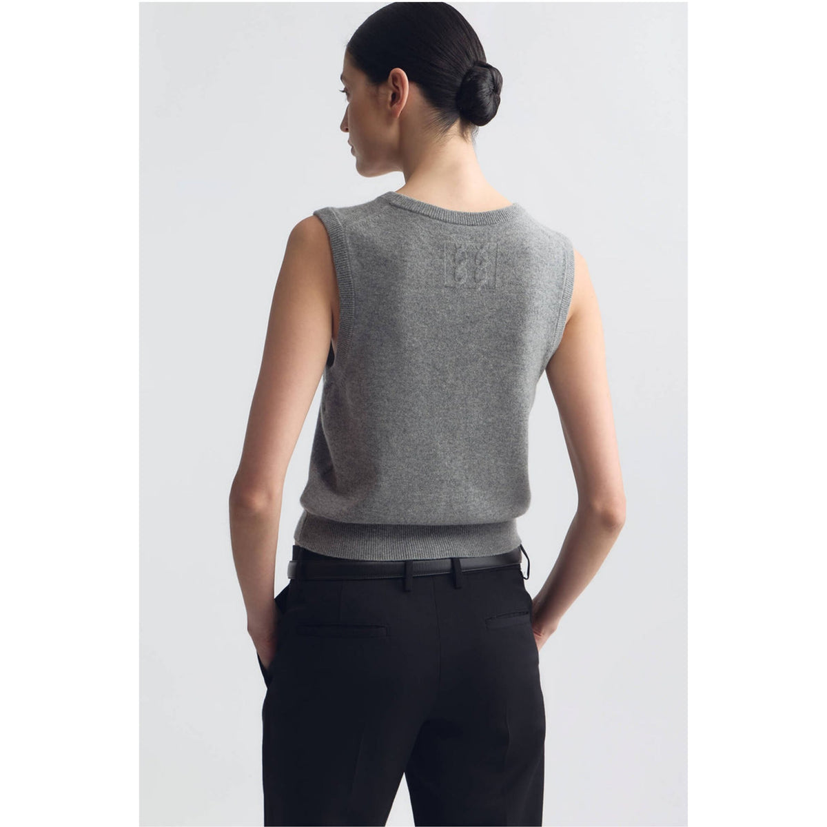 A woman shown from the back wearing a sleeveless heather gray knit top and black trousers against a light gray studio background.