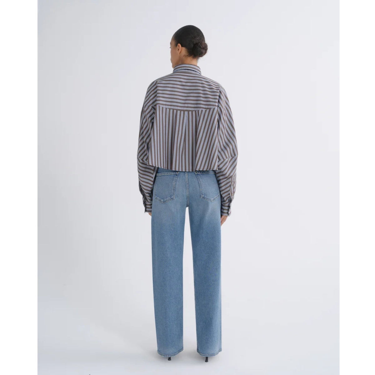 Back view of a model with hair styled in a bun wearing a striped long-sleeve top and high-waisted AGOLDE Ren Jeans in Measure against a light gray background.