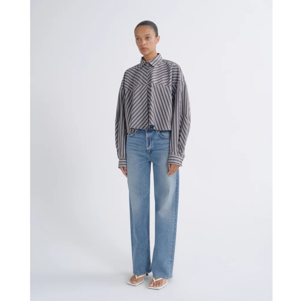 Full-length front view of a model wearing a striped button-up shirt and AGOLDE Ren Jeans in Measure against a light gray background.