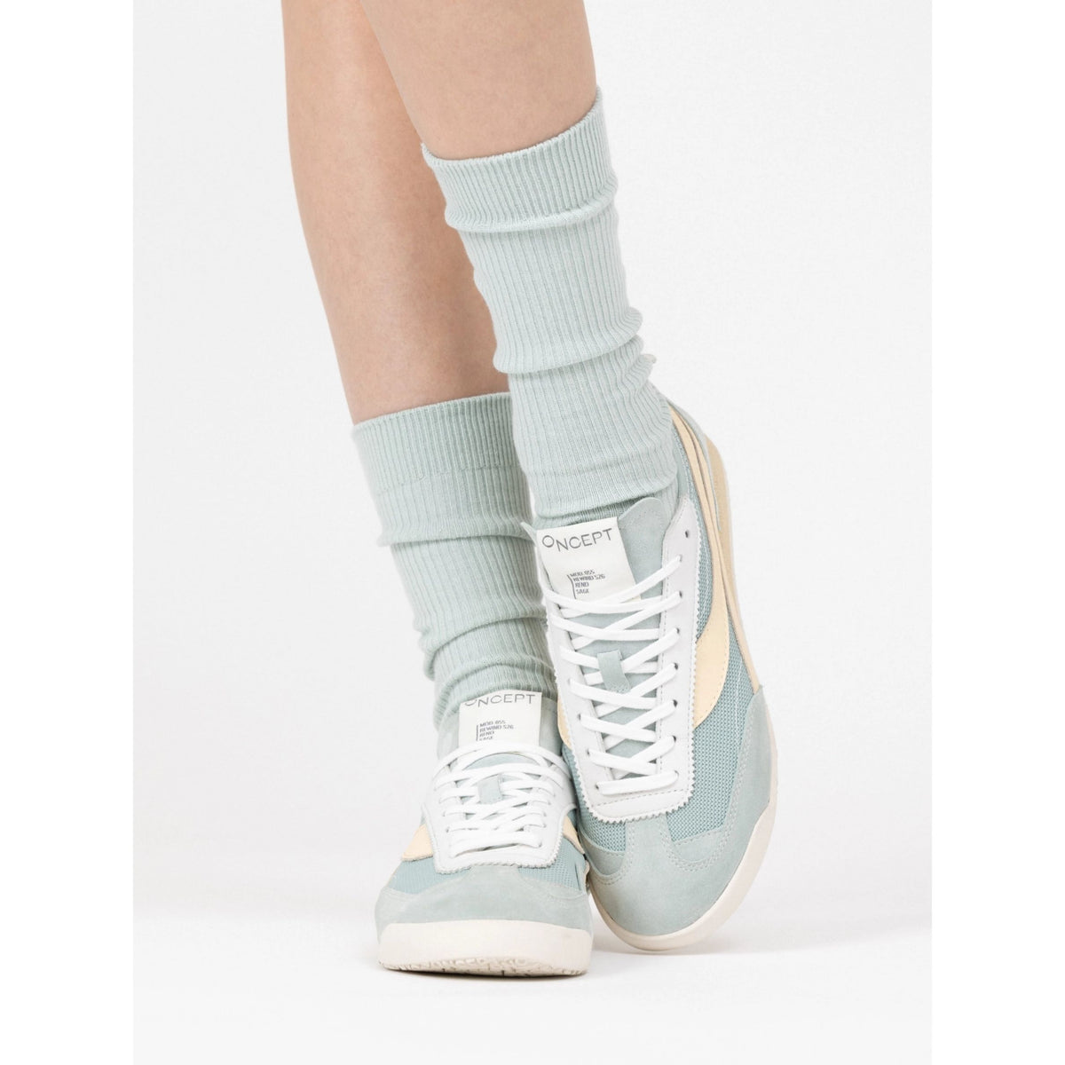 A person wearing light blue ribbed crew socks and matching light blue sneakers with white laces and cream side panels, photographed against a clean white studio background.