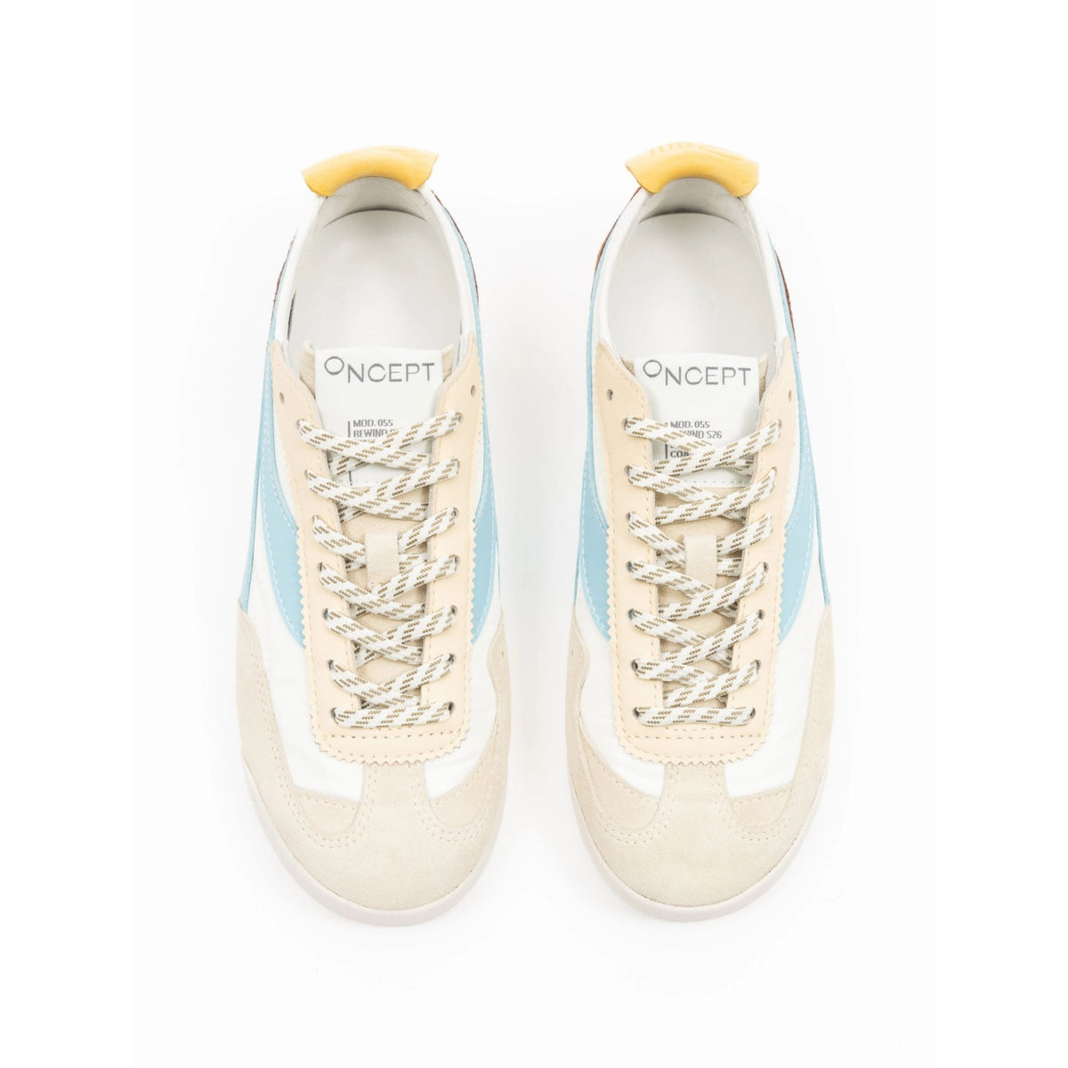 A pair of Oncept low-top sneakers shown from a top-down view on a white background. The sneakers feature a cream suede upper, white leather panels, light blue side stripes, white rope laces, and a small yellow pull tab at the heel.