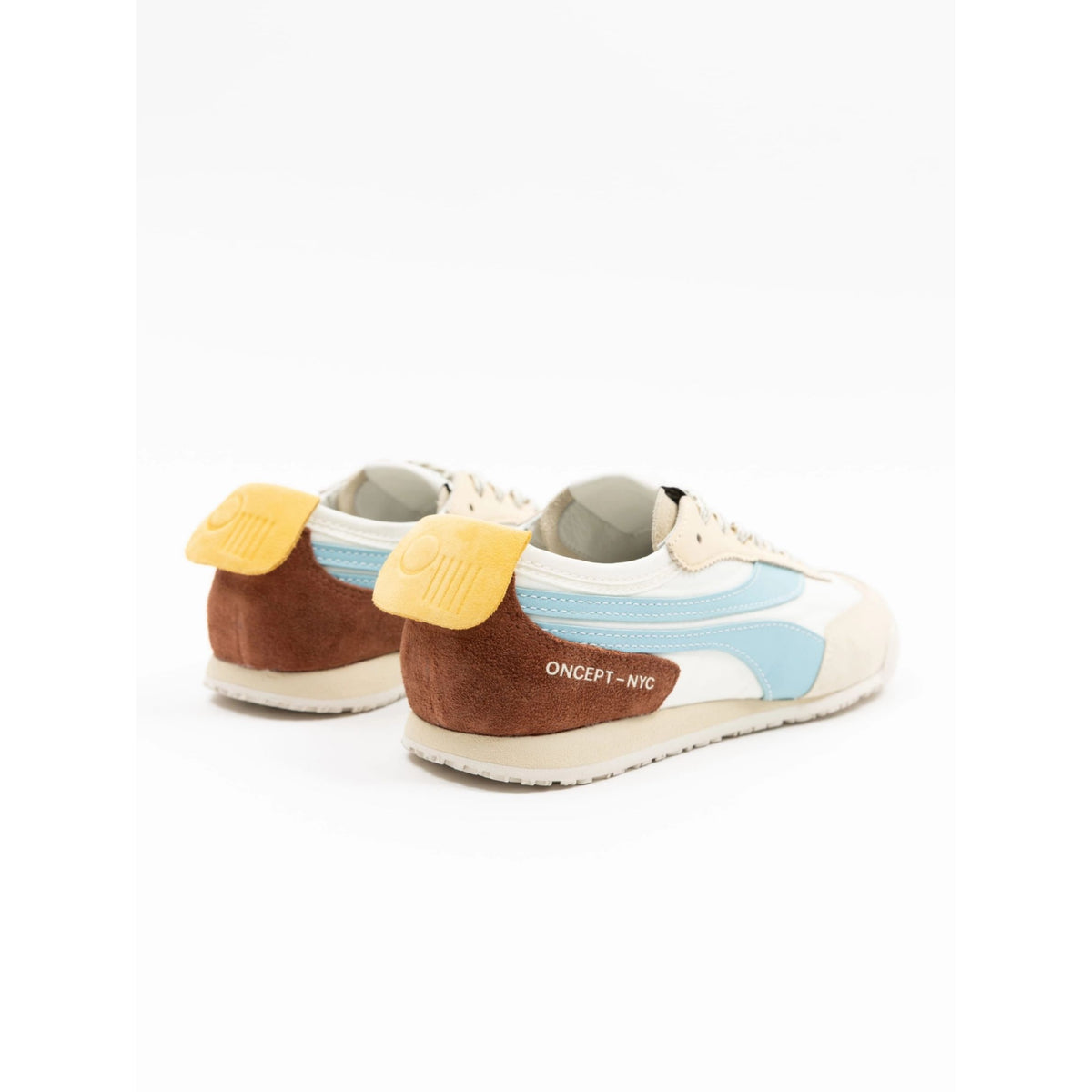 A pair of low-top sneakers shown from the rear three-quarter angle on a white background. The shoes feature a cream-colored leather upper with light blue mesh panels, a brown suede heel section, and bright yellow heel pull tabs.