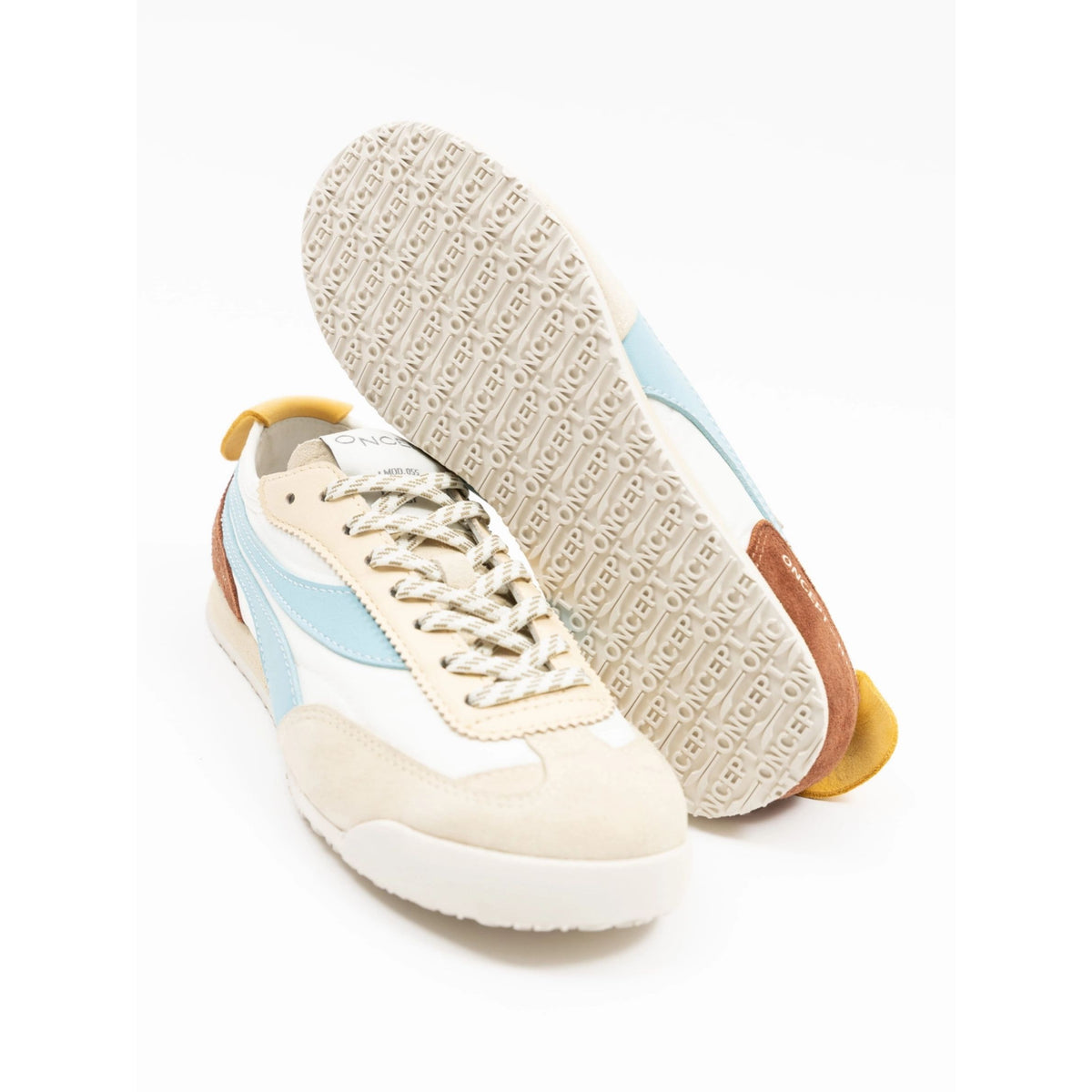 A pair of low-top sneakers shown on a clean white background, with one shoe standing upright to display the textured outsole and the other lying on its side showing the side profile. The shoes feature cream suede and leather panels, white overlays, light blue side stripes, a brown heel tab, and a yellow pull tab.