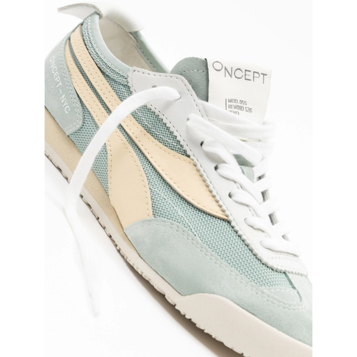 A close-up of a Oncept sneaker in pale sage green, cream, and white, showing the side paneling, white laces, and the Oncept brand tag.