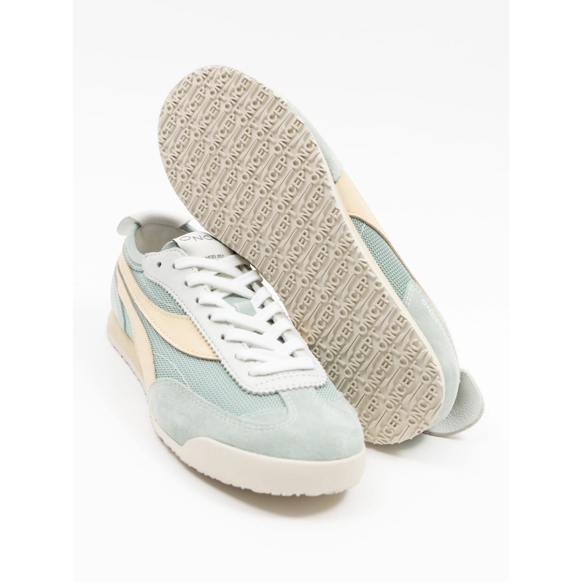 A pair of low-top sneakers in pale mint green, cream, and white, with one shoe standing upright to show the textured beige outsole and the other lying on its side showing the side profile.