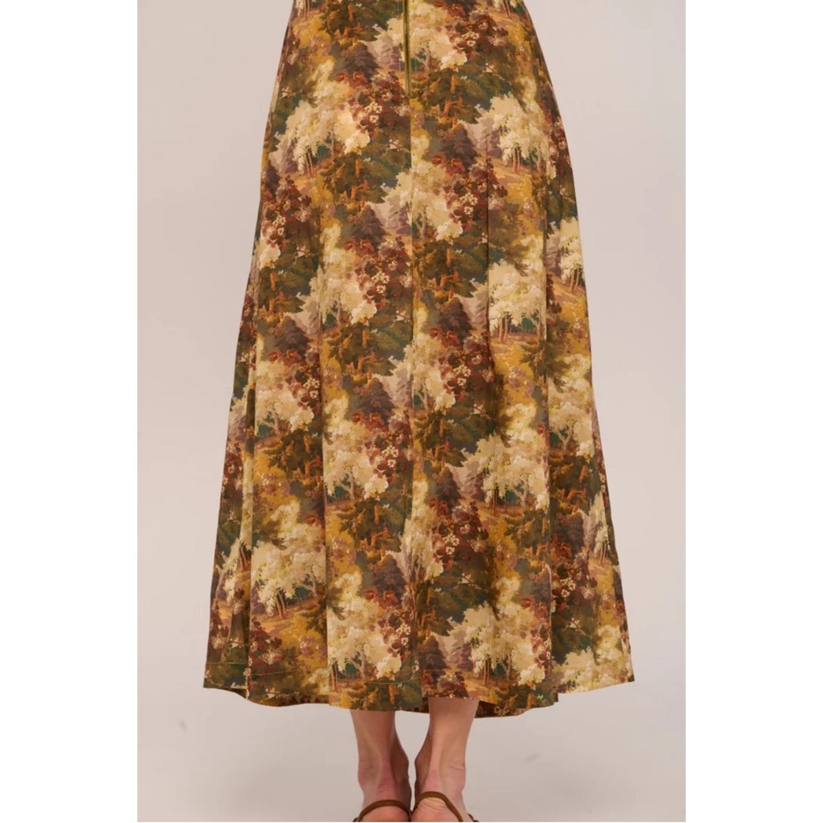 A long A-line midi skirt with a dense floral and botanical print in earthy tones of olive green, mustard yellow, brown, and cream, shown on a model from the waist down.