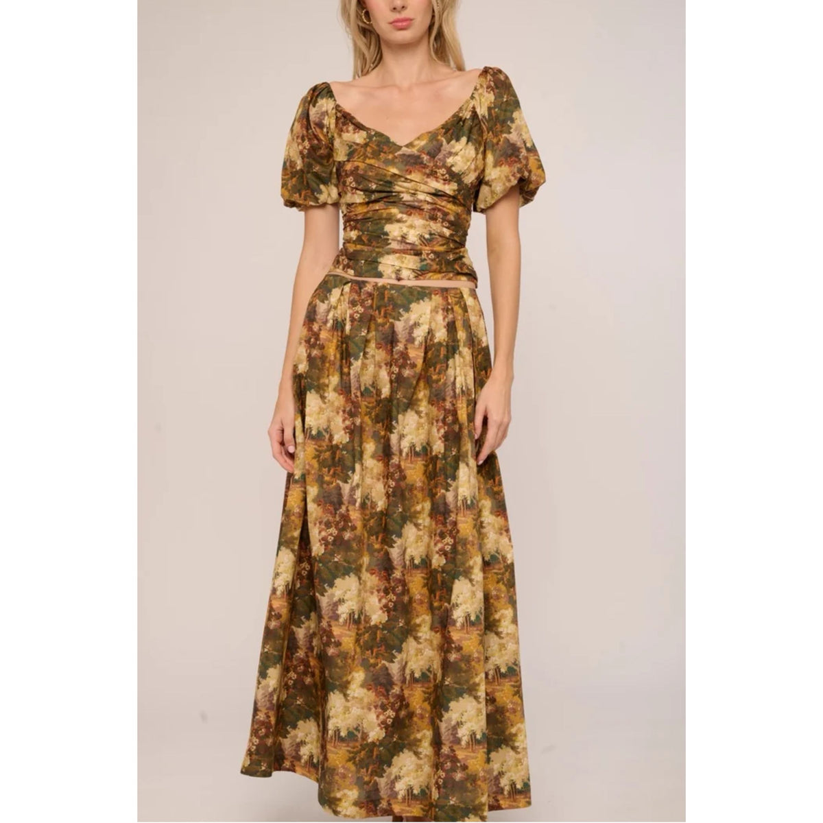 A woman modeling a long floral maxi dress with short puff sleeves, a V-neckline, and a gathered waist, shown against a plain light beige studio background.