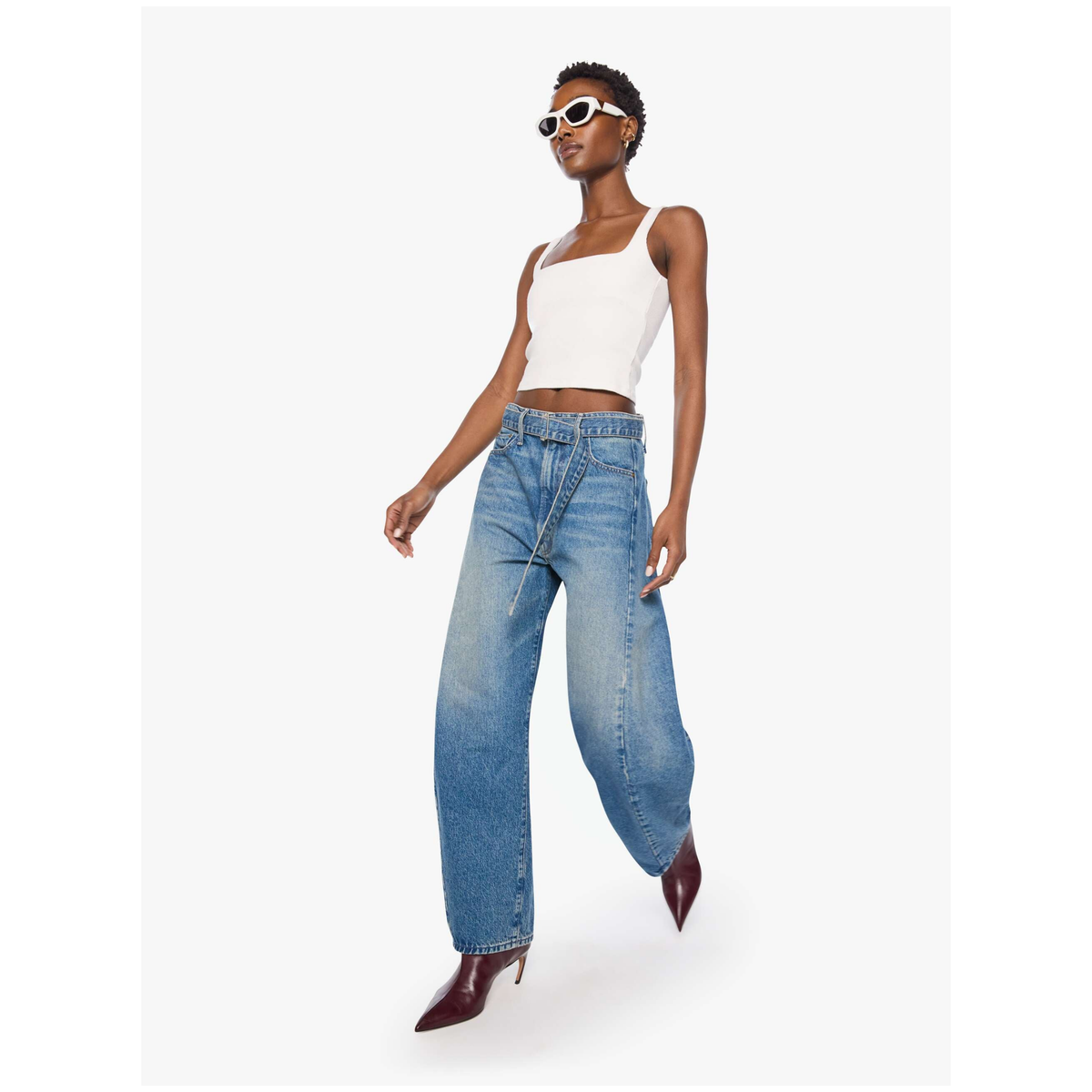 A model wearing a white ribbed crop top, wide-leg blue denim jeans, and dark red pointed-toe heels, posed against a light gray studio background.