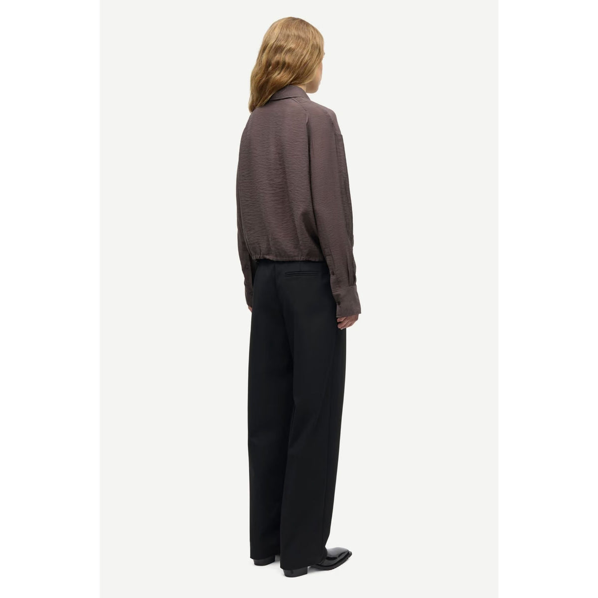 A model shown from the back wearing a dark brown textured long-sleeve shirt and black wide-leg trousers, standing against a plain off-white background.