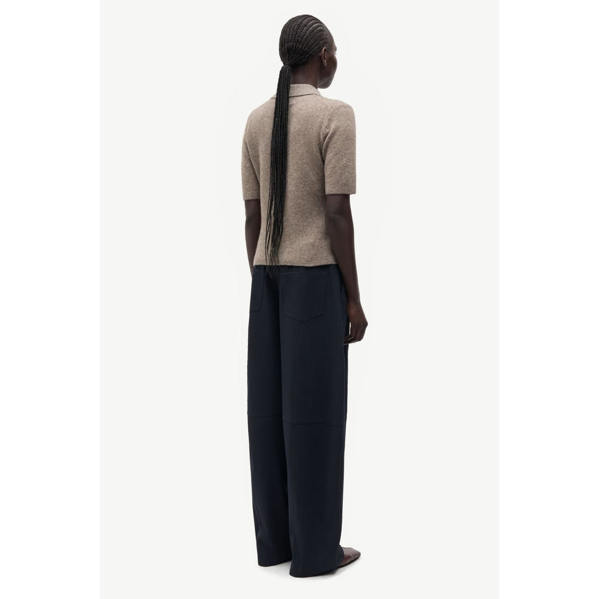 A model shown from the back wearing a beige short-sleeve knit top and dark navy wide-leg trousers, set against a plain off-white background.